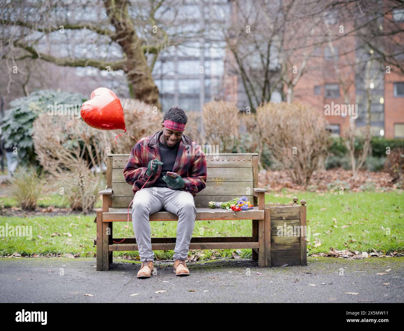 Homme souriant avec ballon en forme de coeur assis sur le banc Banque D'Images