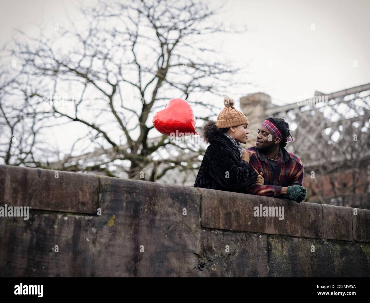 Couple souriant avec ballon en forme de coeur appuyé sur le mur Banque D'Images