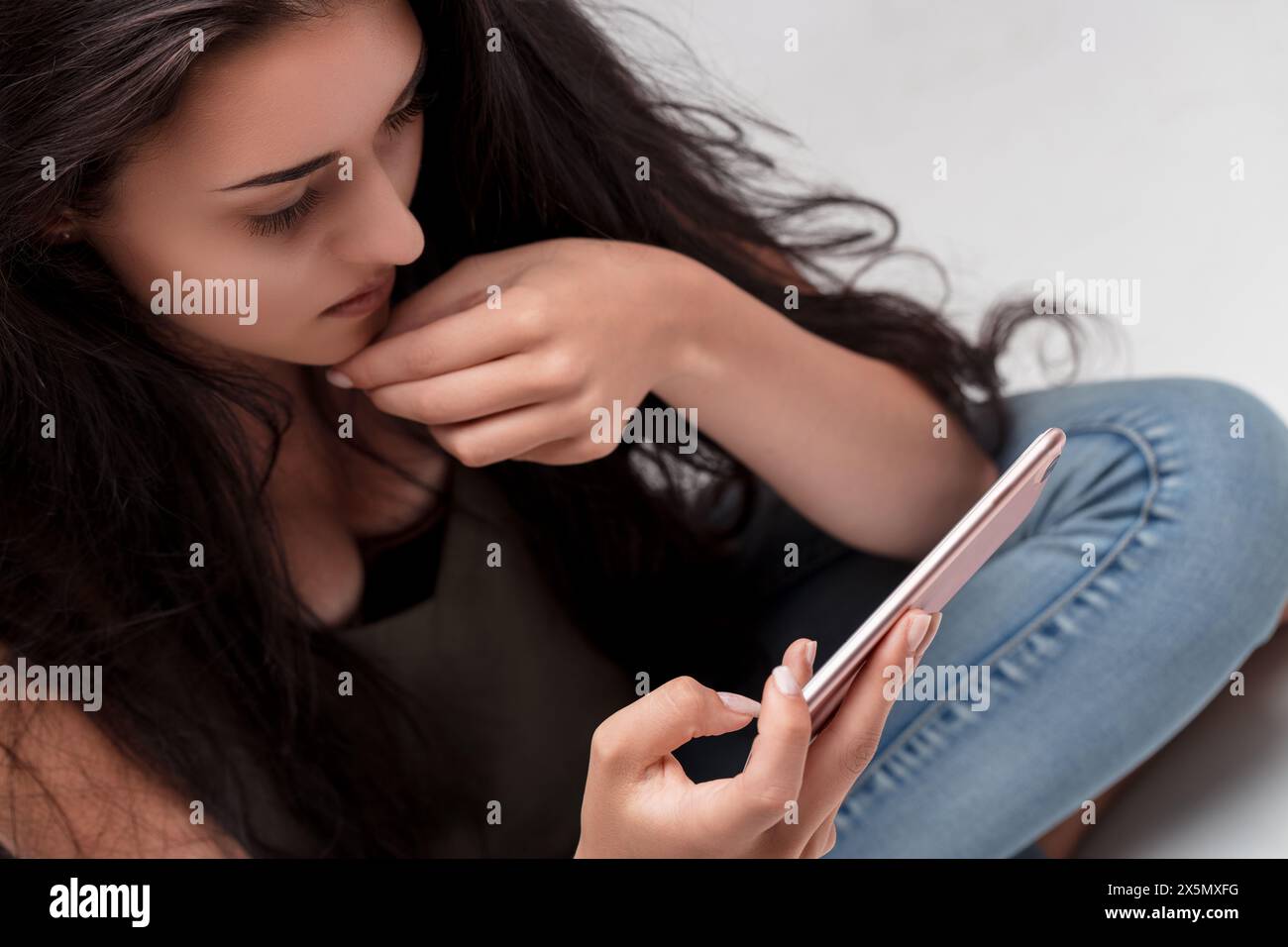 Jeune femme contemplative interagit avec son smartphone, sa pose détendue et son regard intensément concentré Banque D'Images