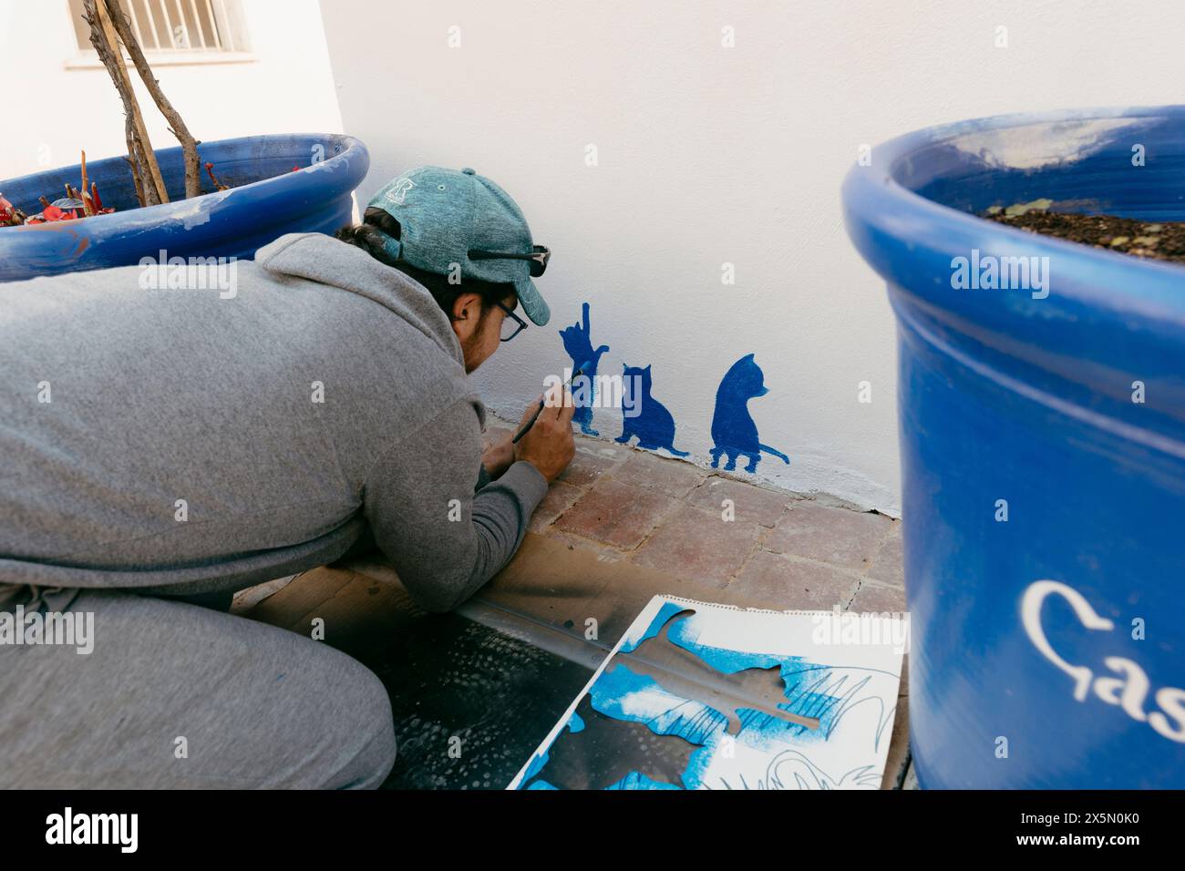 Homme adulte caucasien peignant trois petits chats décoratifs sur un bâtiment de maison de tourisme Banque D'Images