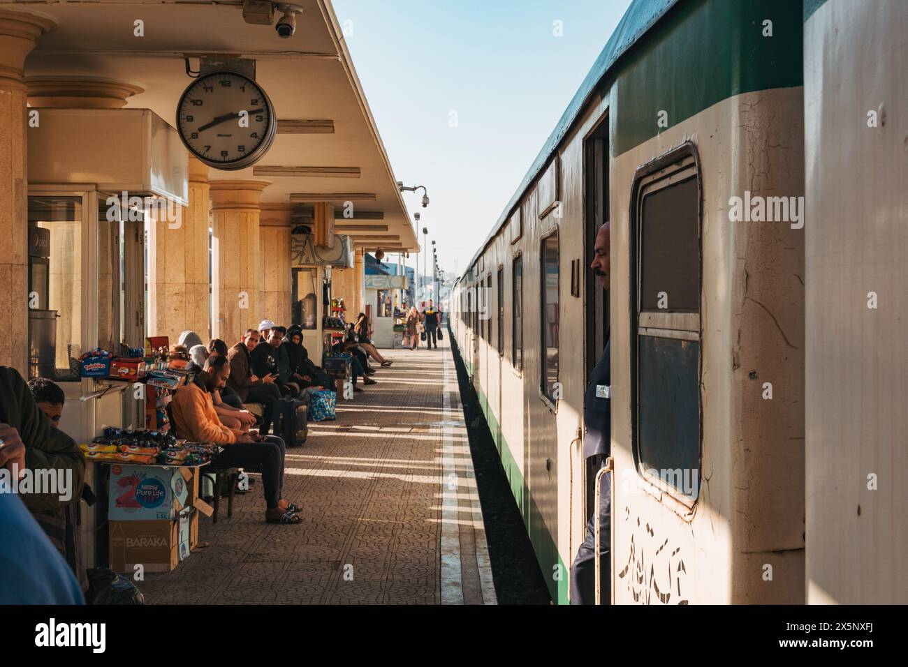 Les passagers attendent et les vendeurs vendent des collations alors qu'un train des chemins de fer égyptiens arrive à la gare de Louxor, en Égypte Banque D'Images