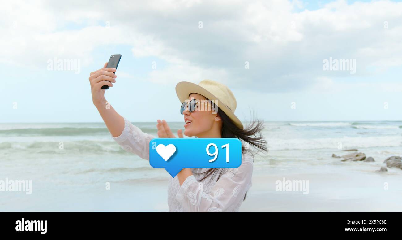Image de cœurs et réactions des médias sociaux sur la femme caucasienne heureuse prenant des photos sur la plage Banque D'Images