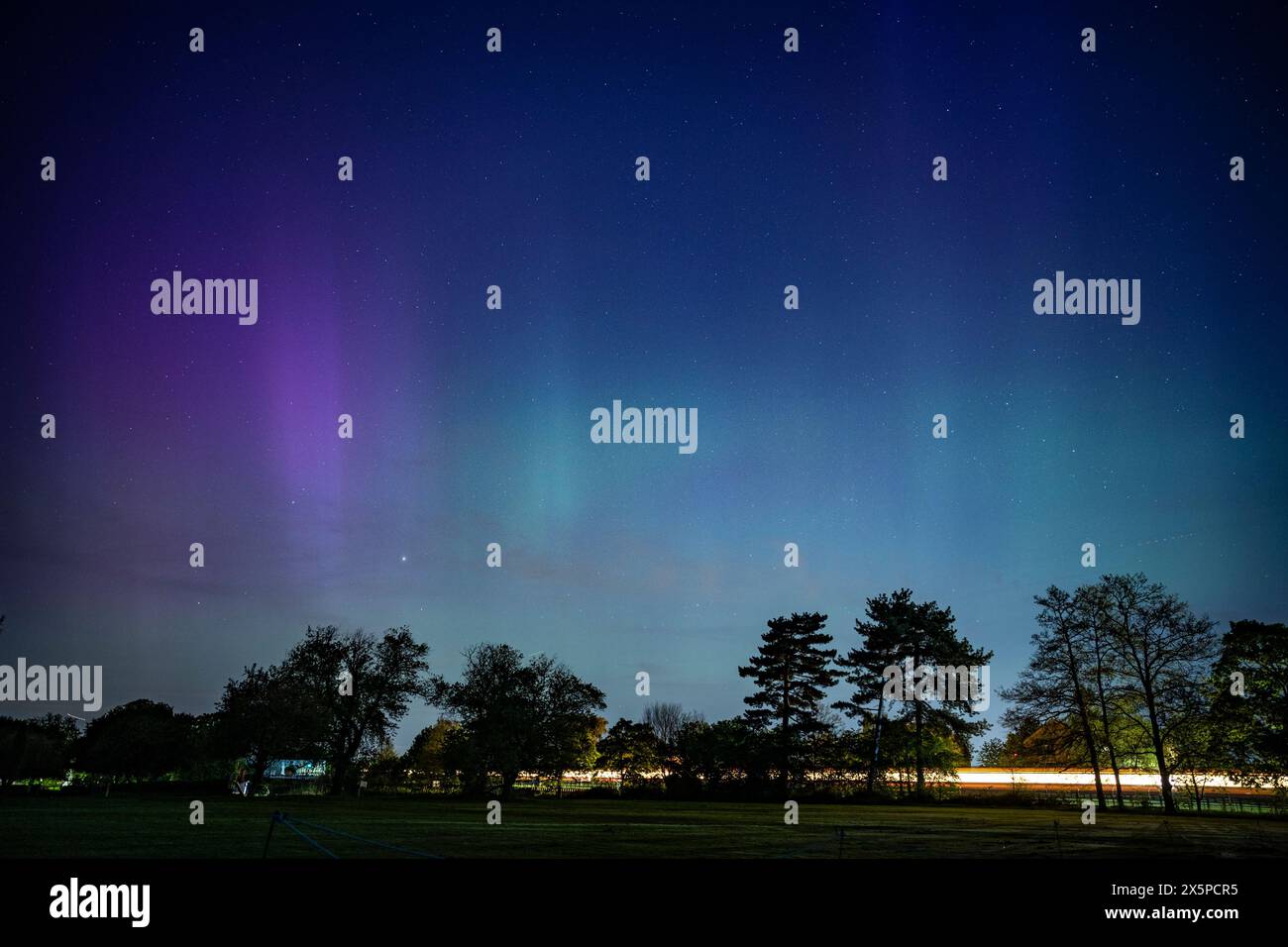 Londres, Royaume-Uni. 11 mai 2024. Météo britannique – Un train de métro passe alors que les aurores boréales (aurores boréales) sont vues au-dessus de Northwood, dans le nord-ouest de Londres. Les tempêtes géomagnétiques les plus fortes depuis des années frappent la terre et un rare avertissement de tempête solaire a été émis, augmentant les chances de voir les aurores boréales, causées par des particules chargées du soleil heurtant les gaz dans l'atmosphère terrestre. Les atomes d'oxygène brillent en vert - la couleur la plus souvent vue dans les aurores boréales, tandis que les atomes d'azote émettent du violet, du bleu et du rose. Credit : Stephen Chung / Alamy Live News Banque D'Images