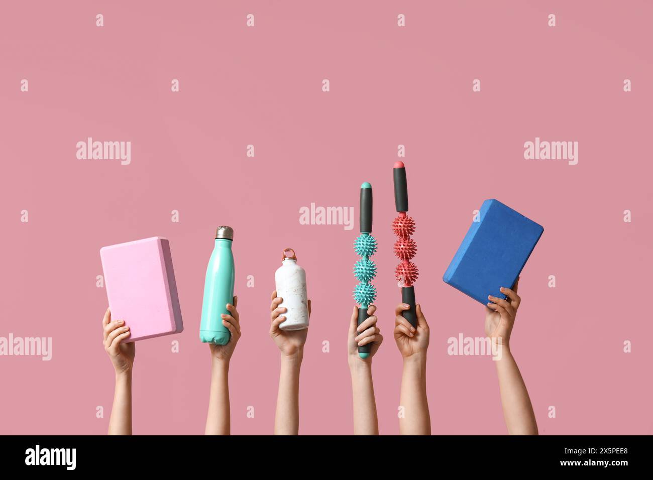 Mains féminines avec des bâtons de massage de rouleau, des blocs de yoga et une bouteille d'eau de sport sur fond rose Banque D'Images