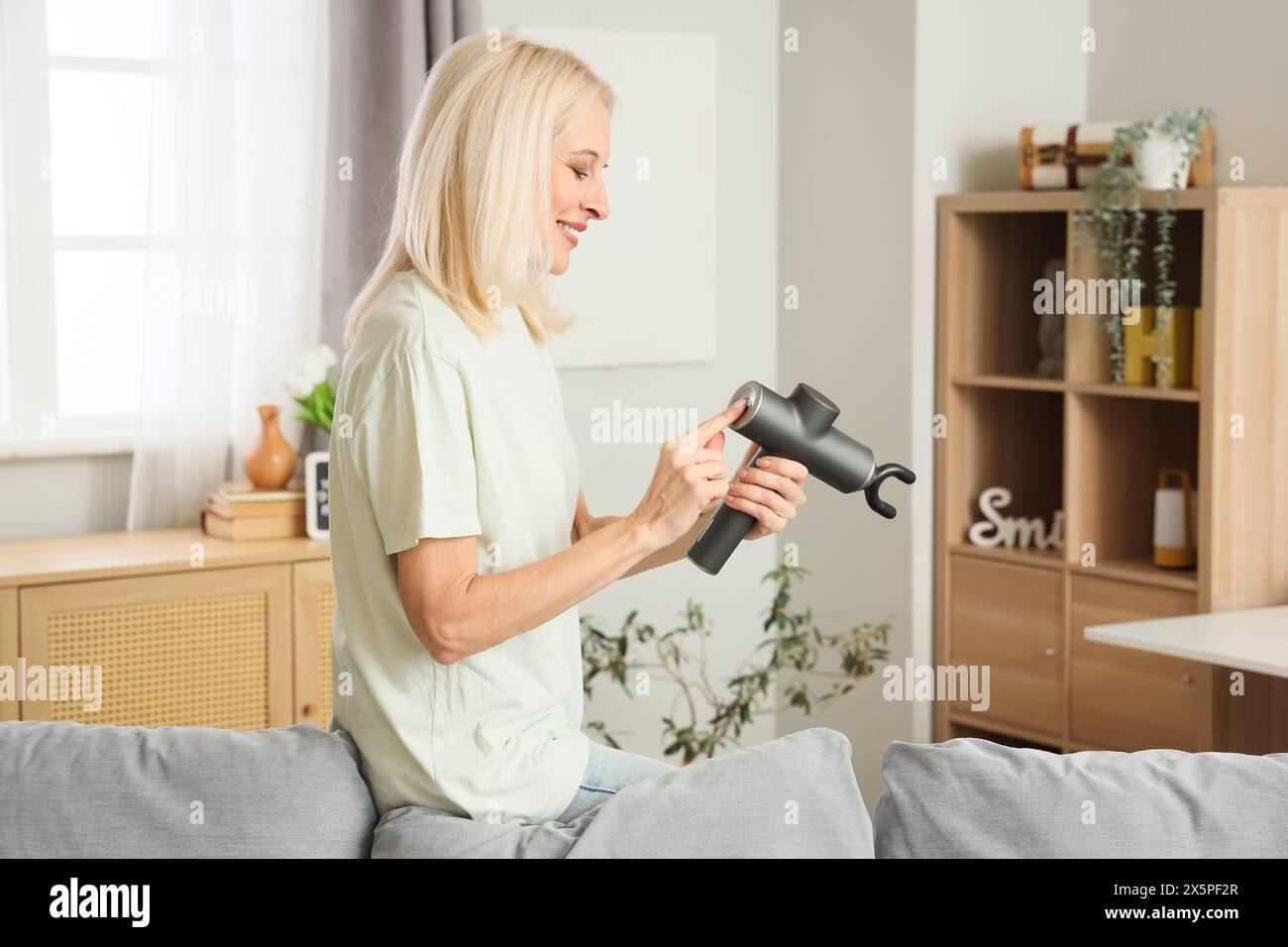 Femme mature avec masseur à percussion à la maison Banque D'Images