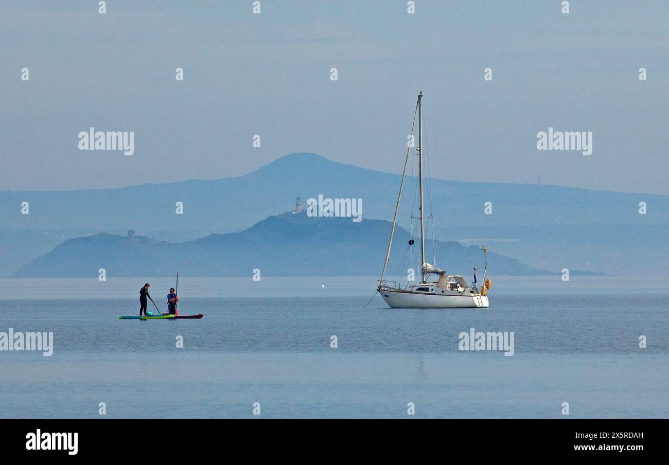 Portobello, Édimbourg, Écosse, Royaume-Uni. 11 mai 2024. Matin brumeux à 14 degrés centigrades pour ceux qui sortent pour exrcise sur la plage et le Firth of Forth. Sur la photo : planches de paddle et yacht de plaisance amarré sur Firth of Forth avec une île brumeuse d'Inchkeith et Lomond Hills en arrière-plan. Credit : Arch White/Alamy Live news. Banque D'Images