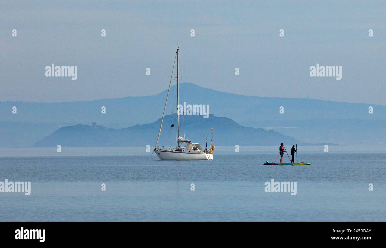 Portobello, Édimbourg, Écosse, Royaume-Uni. 11 mai 2024. Matin brumeux à 14 degrés centigrades pour ceux qui sortent pour exrcise sur la plage et le Firth of Forth. Sur la photo : planches de paddle et yacht de plaisance amarré sur Firth of Forth avec une île brumeuse d'Inchkeith et Lomond Hills en arrière-plan. Credit : Arch White/Alamy Live news. Banque D'Images