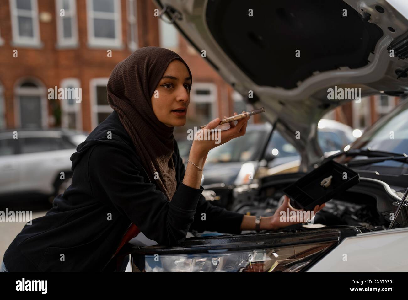 Femme portant le hijab parlant sur le téléphone portable tout en réparant la voiture Banque D'Images