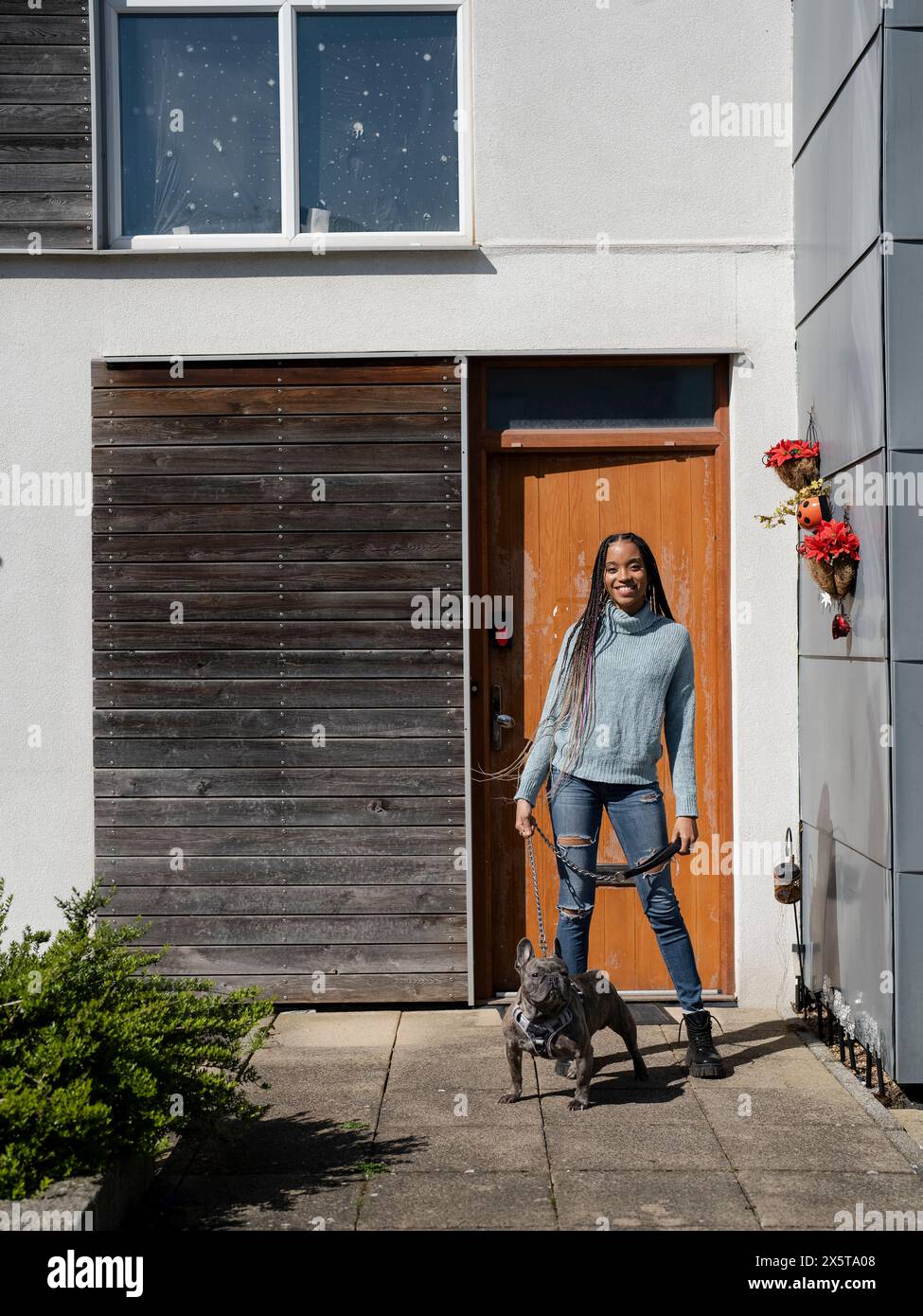 Femme souriante posant avec le chien devant la maison le jour ensoleillé Banque D'Images