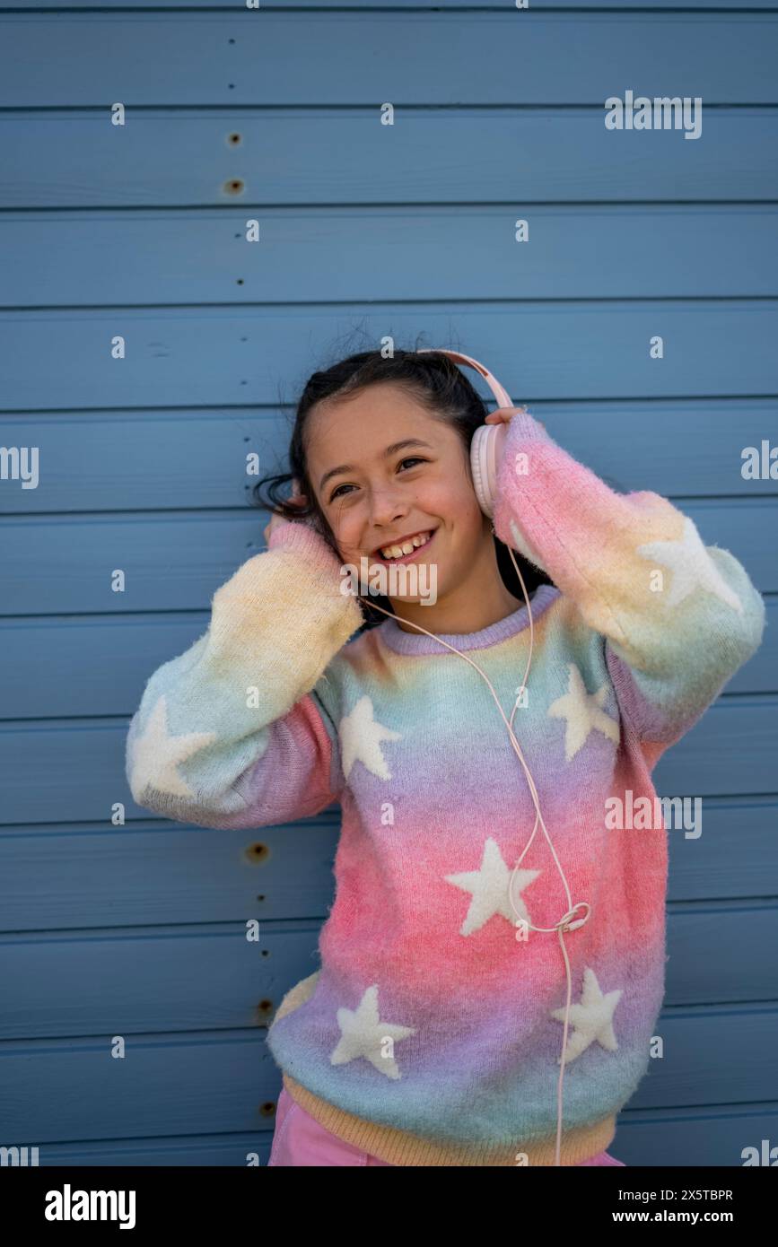 Fille souriante (8-9) dans des vêtements colorés écoutant de la musique à l'extérieur Banque D'Images