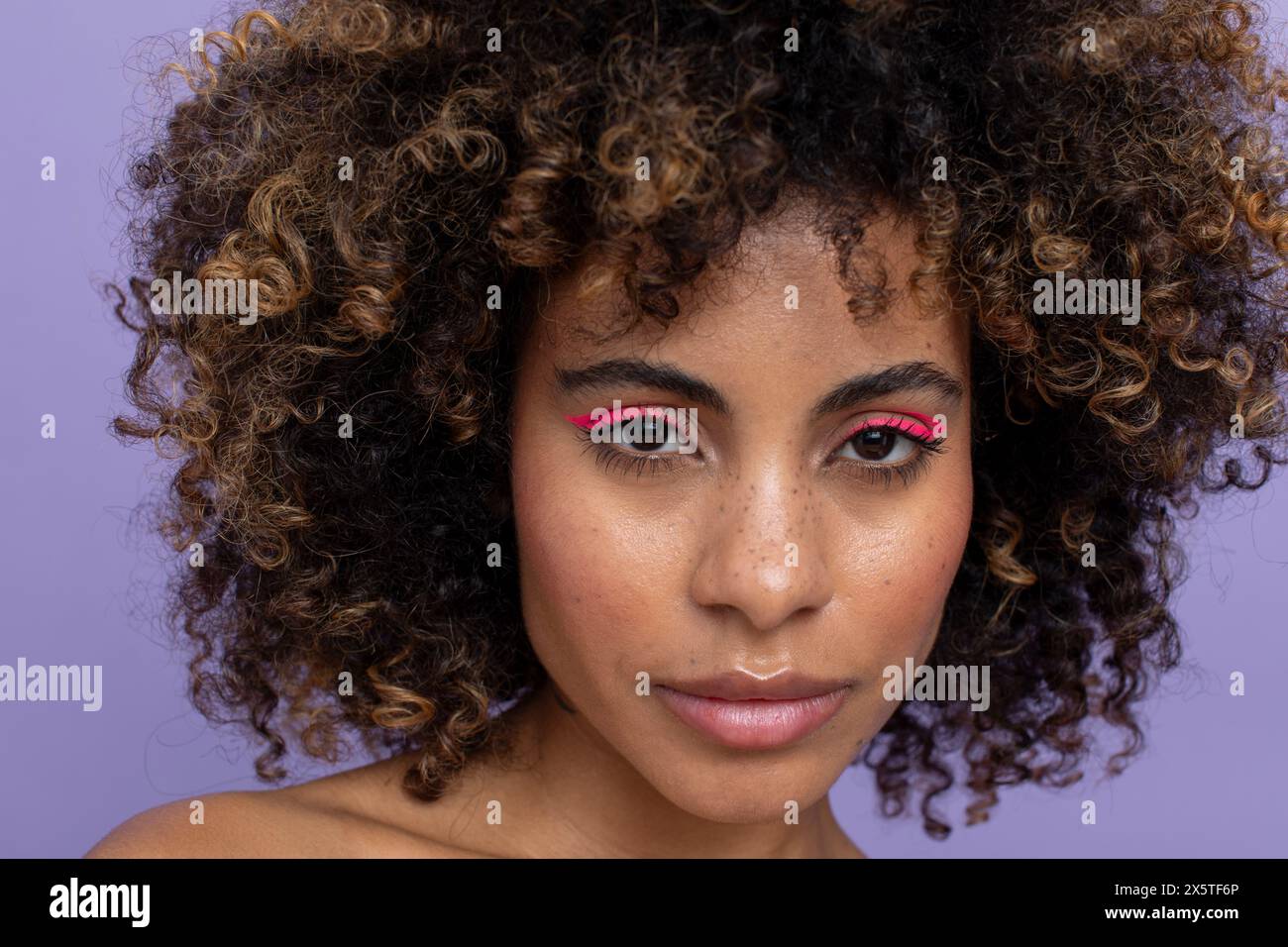 Portrait de femme avec les cheveux bouclés et le maquillage rose regardant la caméra Banque D'Images