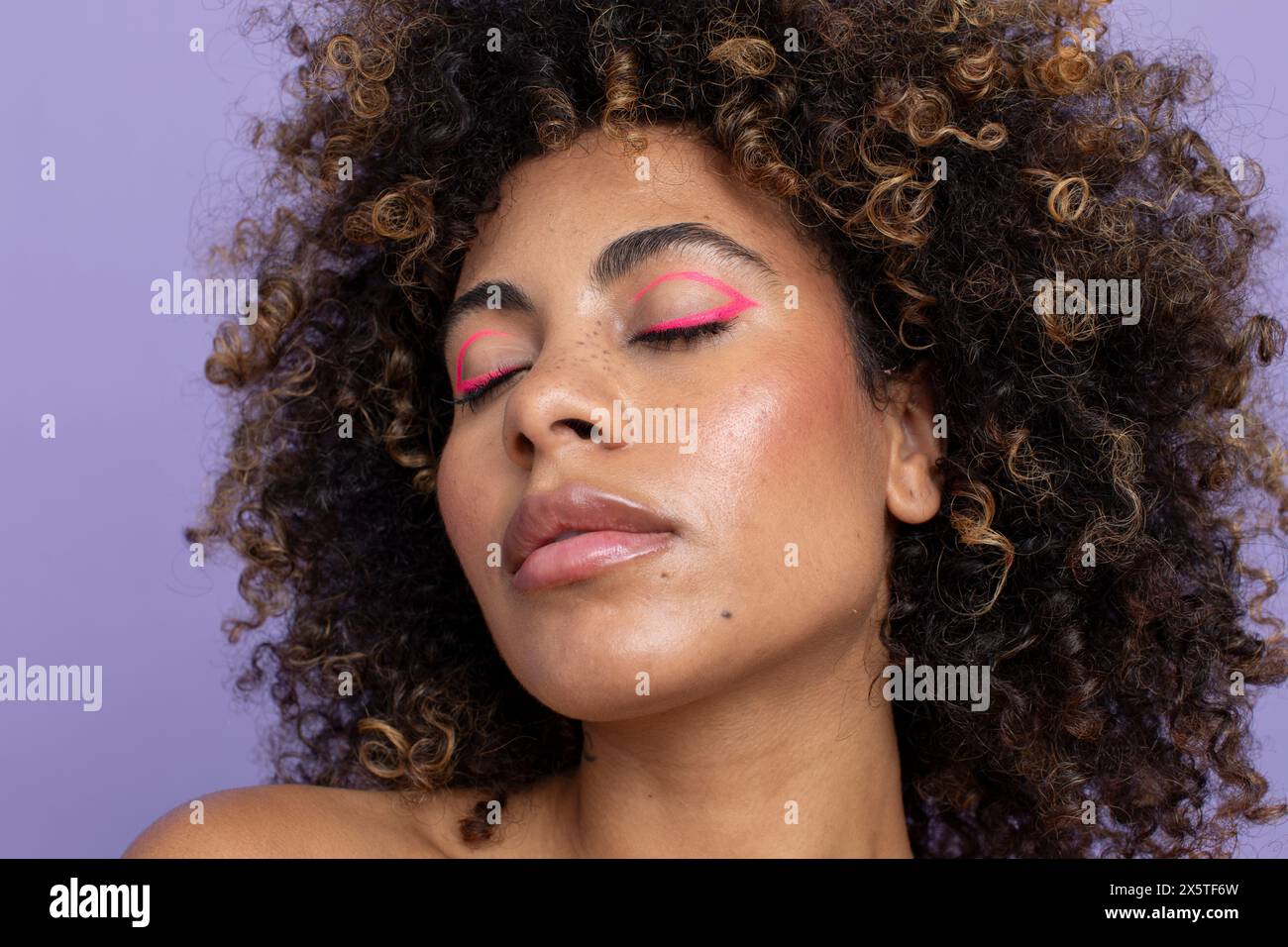 Femme aux cheveux bouclés, yeux fermés et maquillage rose Banque D'Images