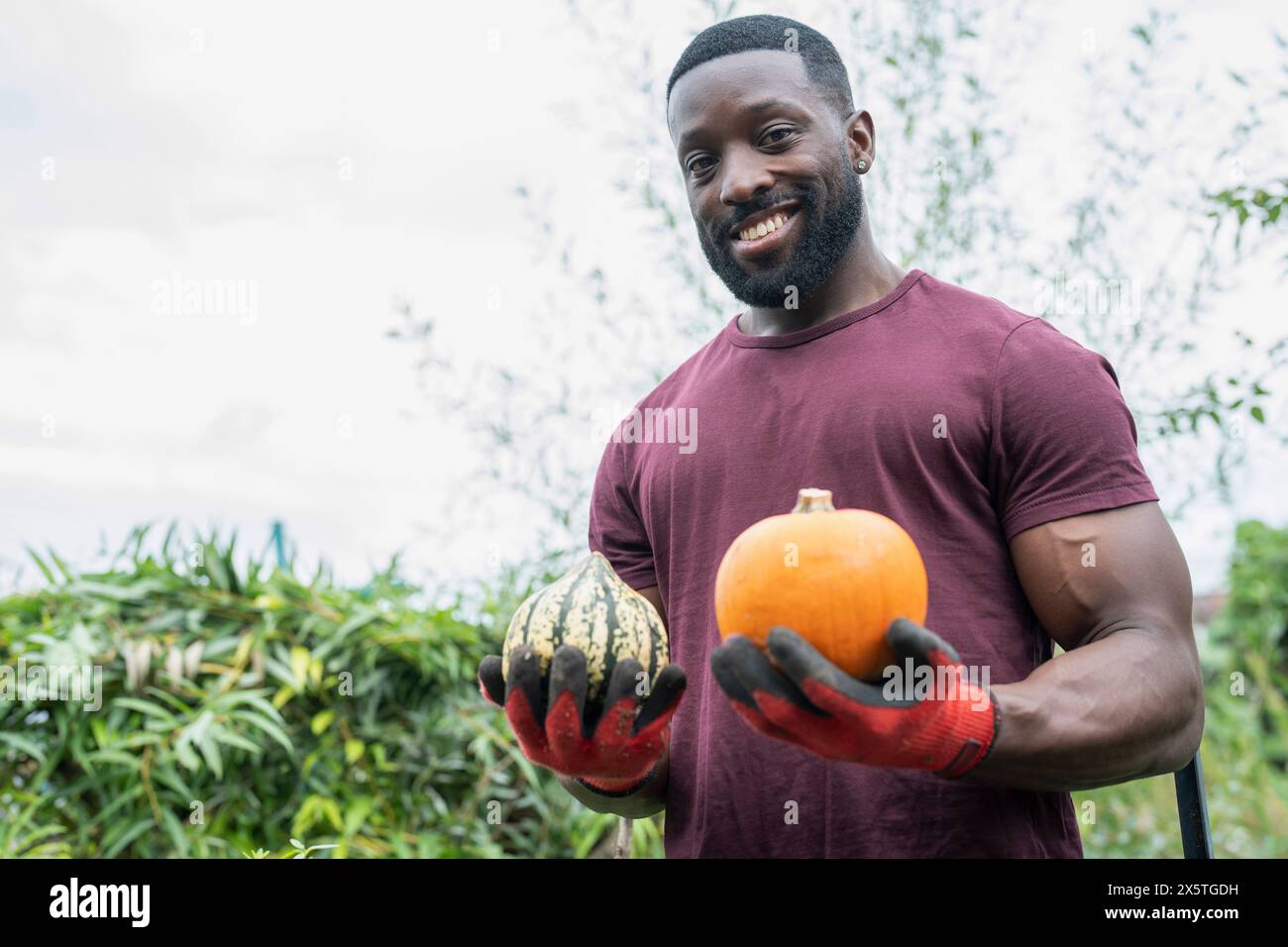 Portrait d'homme souriant tenant des citrouilles dans le jardin urbain Banque D'Images