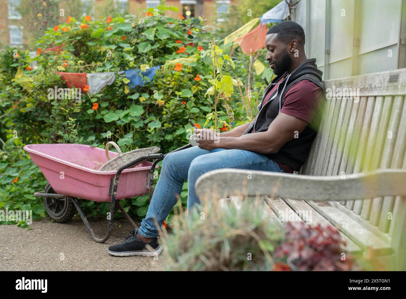 Homme avec téléphone intelligent assis sur le banc dans l'allotissement Banque D'Images