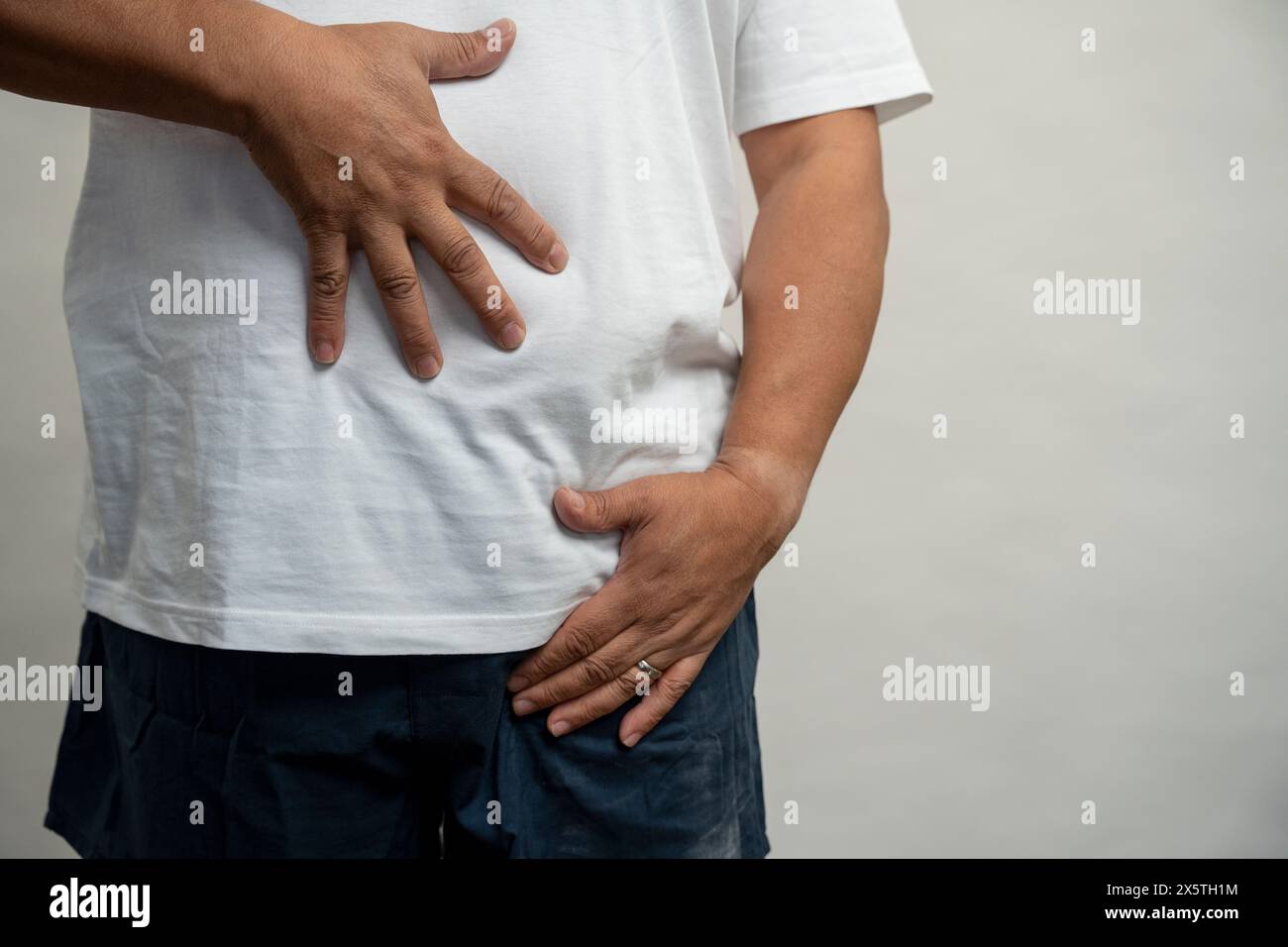 Homme avec les mains sur le ventre sur fond gris Banque D'Images