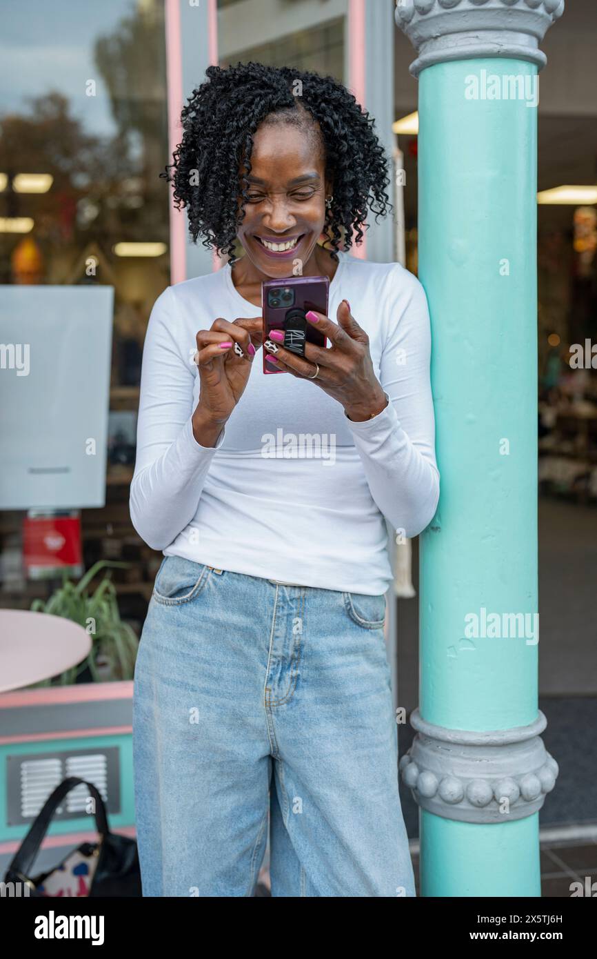 Femme souriante utilisant un smartphone devant le bâtiment Banque D'Images