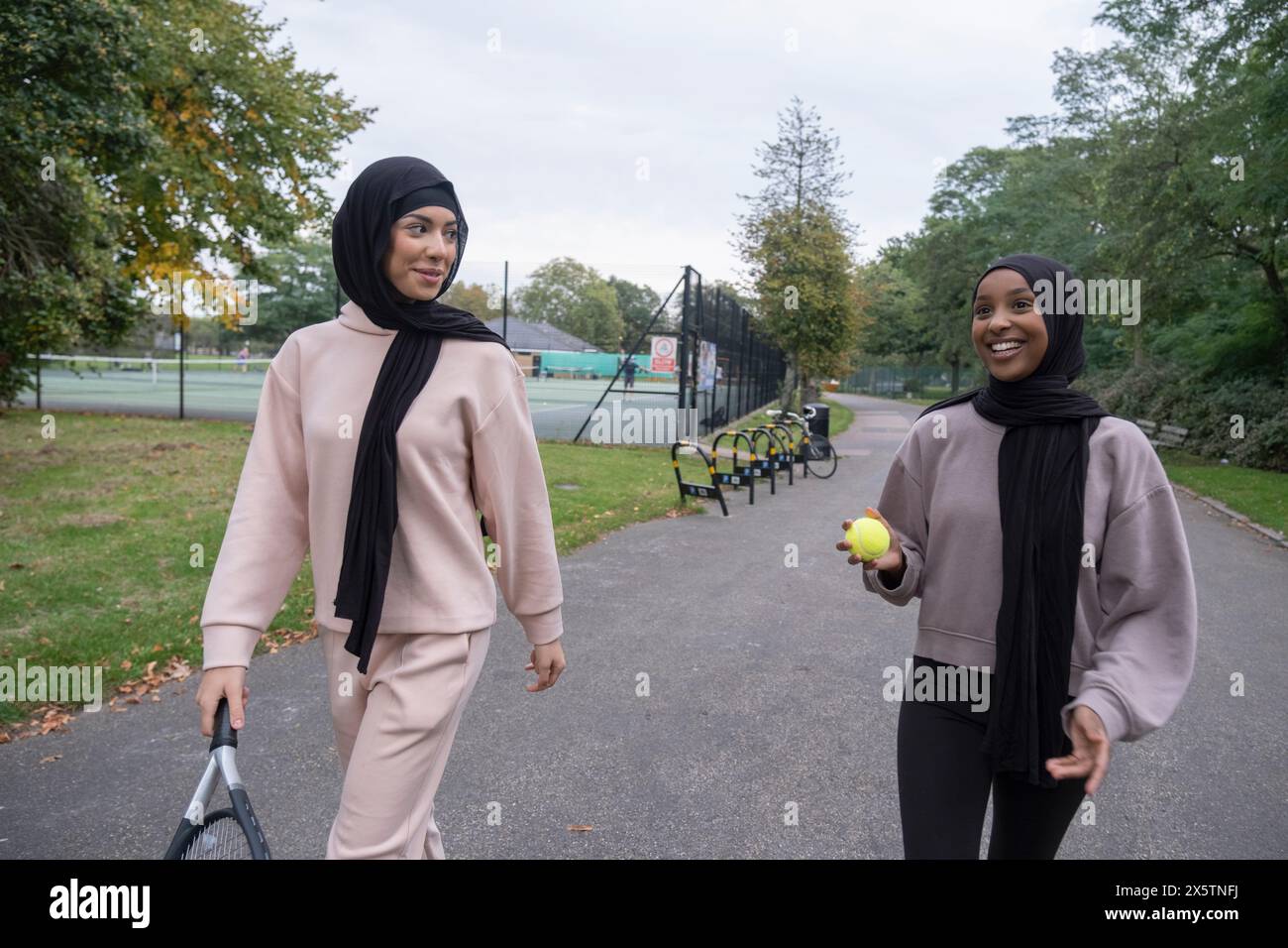 Deux femmes en hijabs marchant dans le parc avec raquette de tennis et balle Banque D'Images