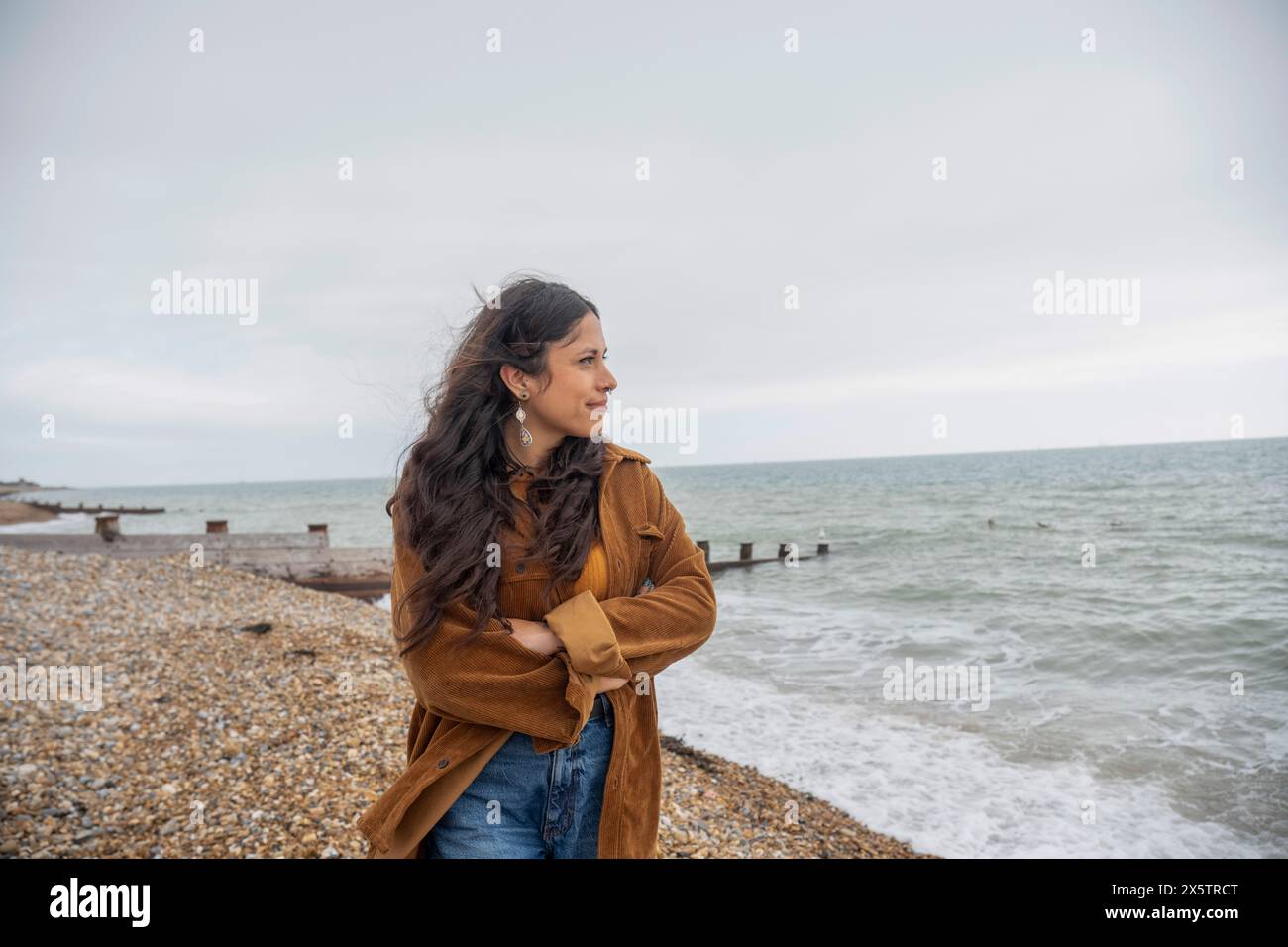 Femme réfléchie regardant la mer tout en se tenant sur la plage un jour nuageux Banque D'Images