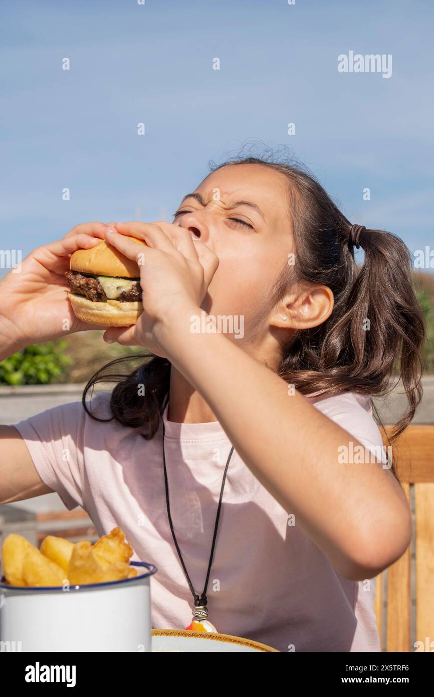 Fille mangeant un hamburger le jour ensoleillé Banque D'Images