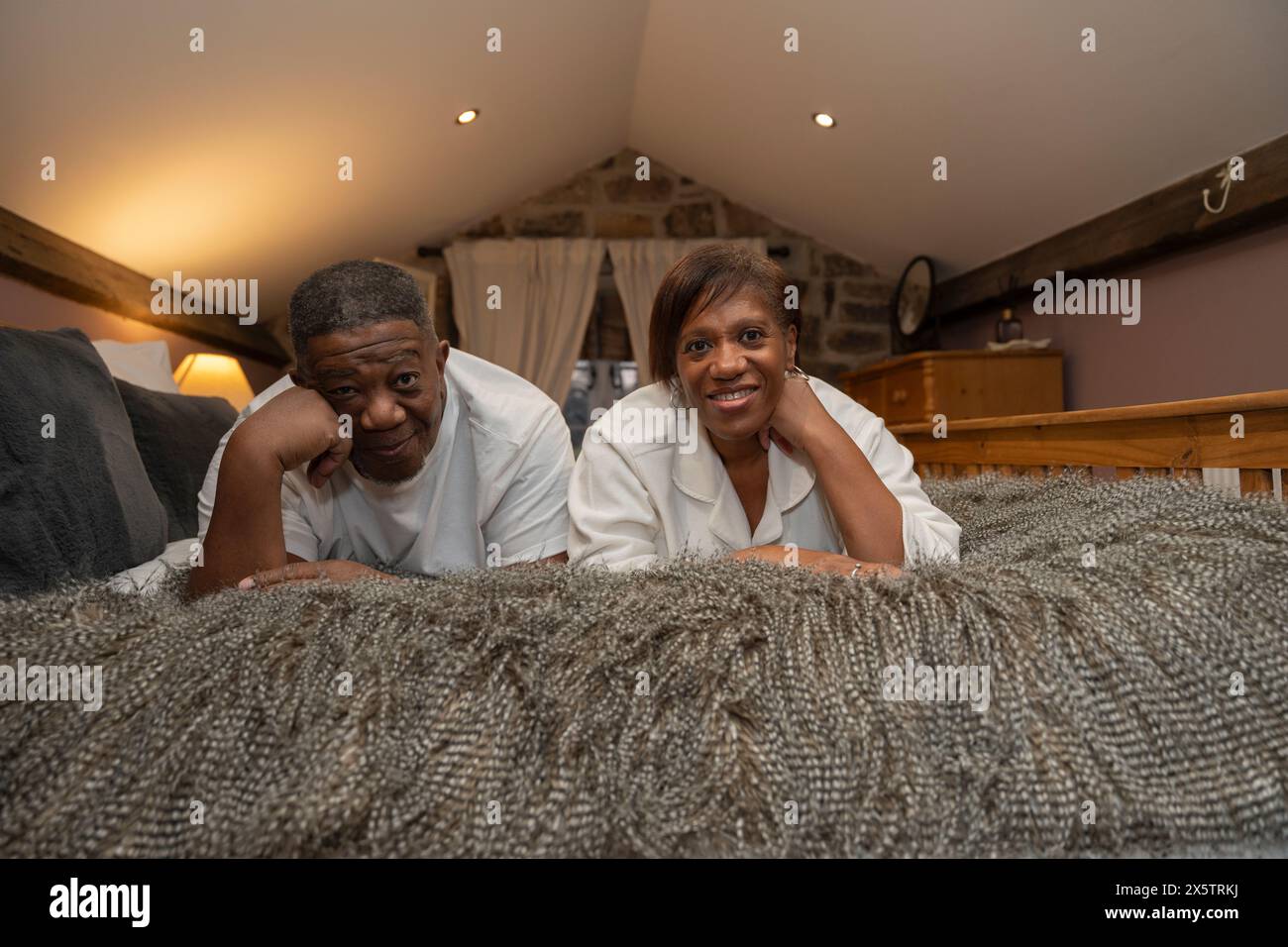 Couple senior souriant allongé sur le devant dans la chambre, regardant la caméra Banque D'Images