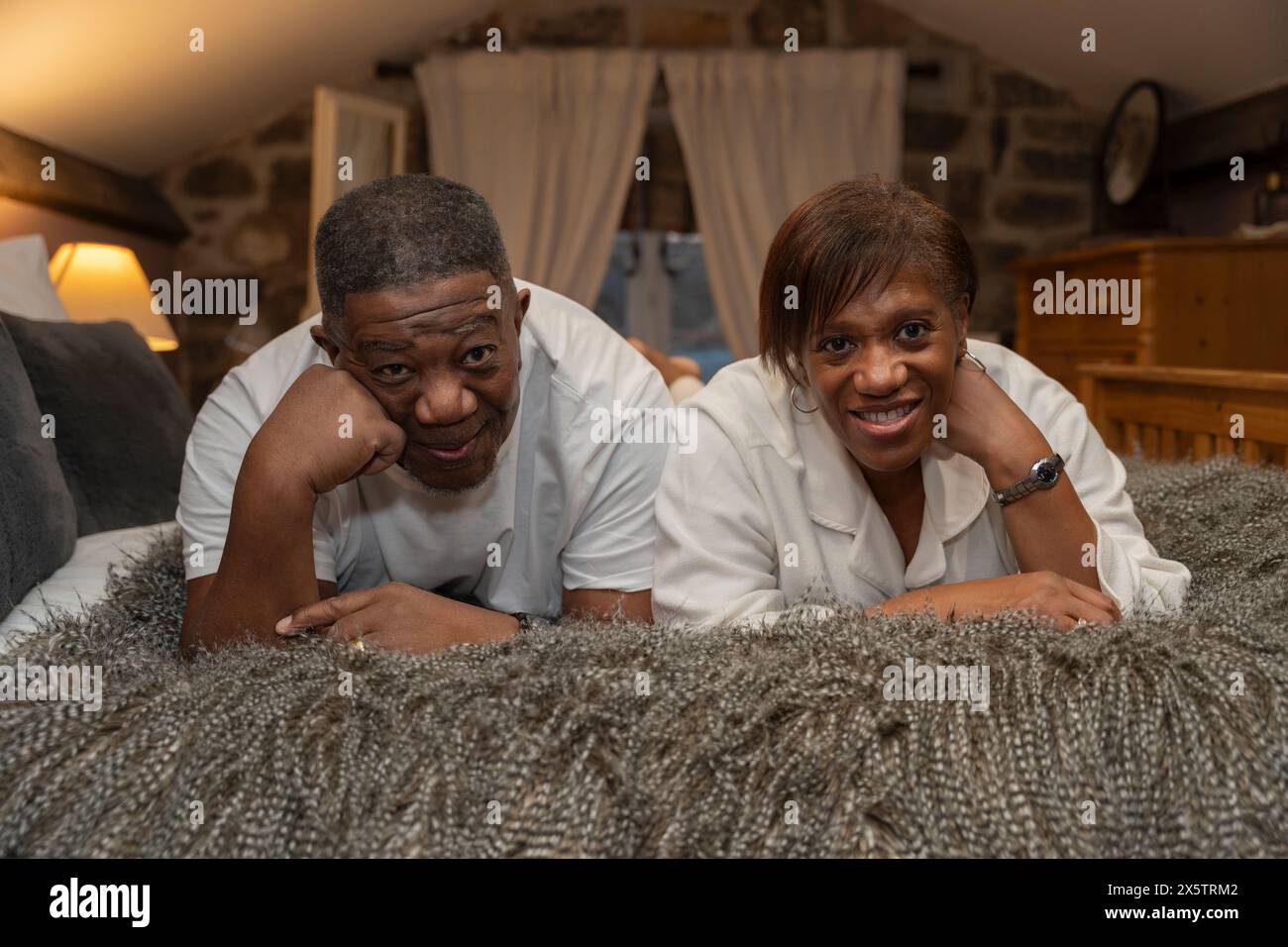 Couple senior souriant allongé sur le devant dans la chambre, regardant la caméra Banque D'Images