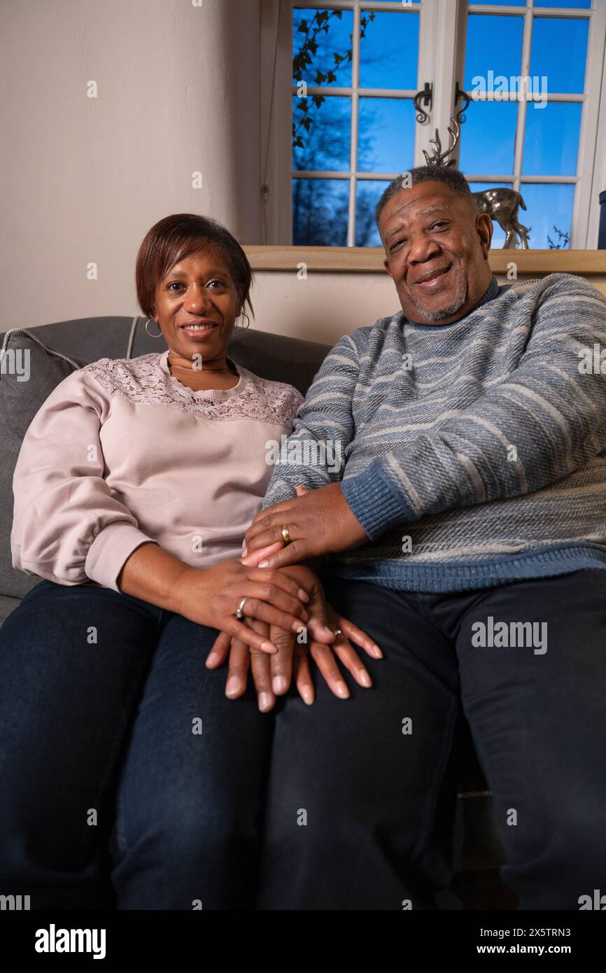 Couple senior assis ensemble, se tenant la main et regardant la caméra Banque D'Images