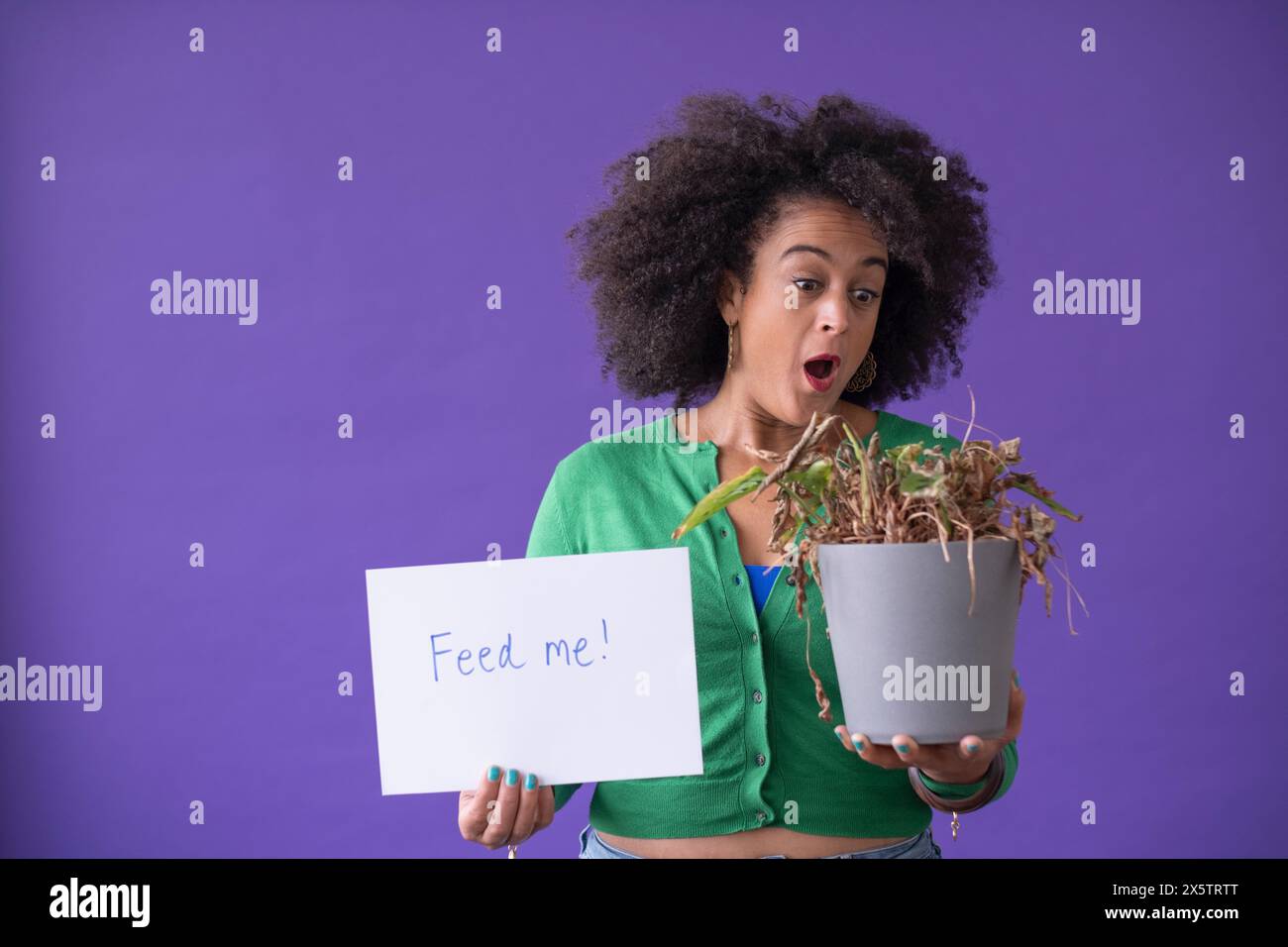 Portrait de studio de femme surprise tenant la plante en pot séchée et signe Banque D'Images