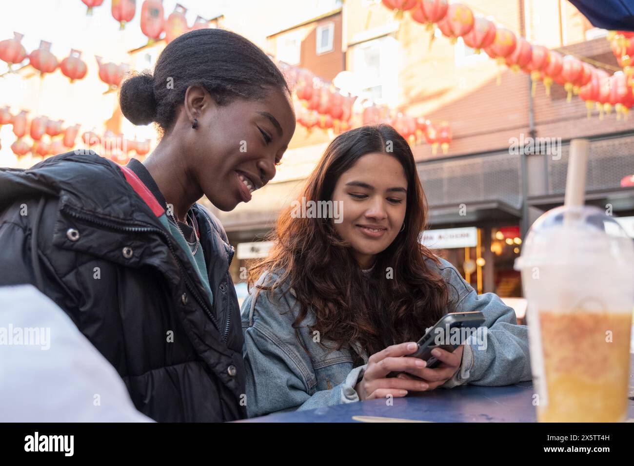 Jeunes femmes vérifiant le téléphone tout en dînant à l'extérieur dans Chinatown Banque D'Images