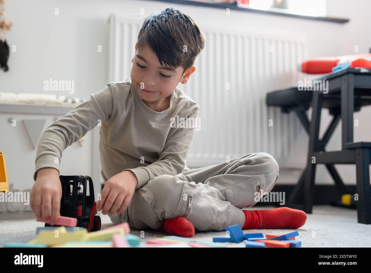 Garçon (6-7) assis sur le sol et jouant avec des jouets Banque D'Images