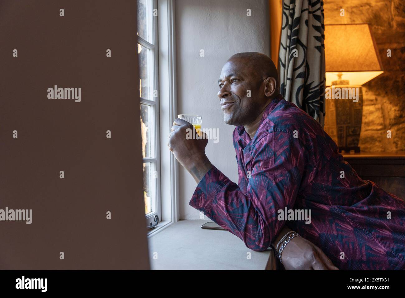 Homme appuyé sur le rebord de la fenêtre avec un verre de jus et regardant par la fenêtre Banque D'Images