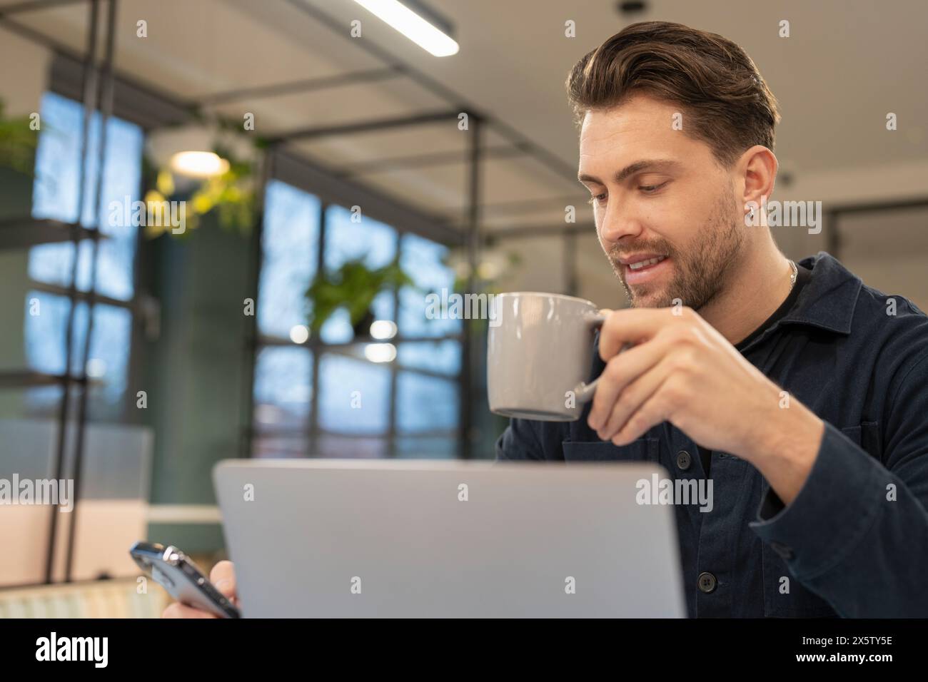 Homme d'affaires utilisant le téléphone et l'ordinateur portable dans le bureau moderne Banque D'Images