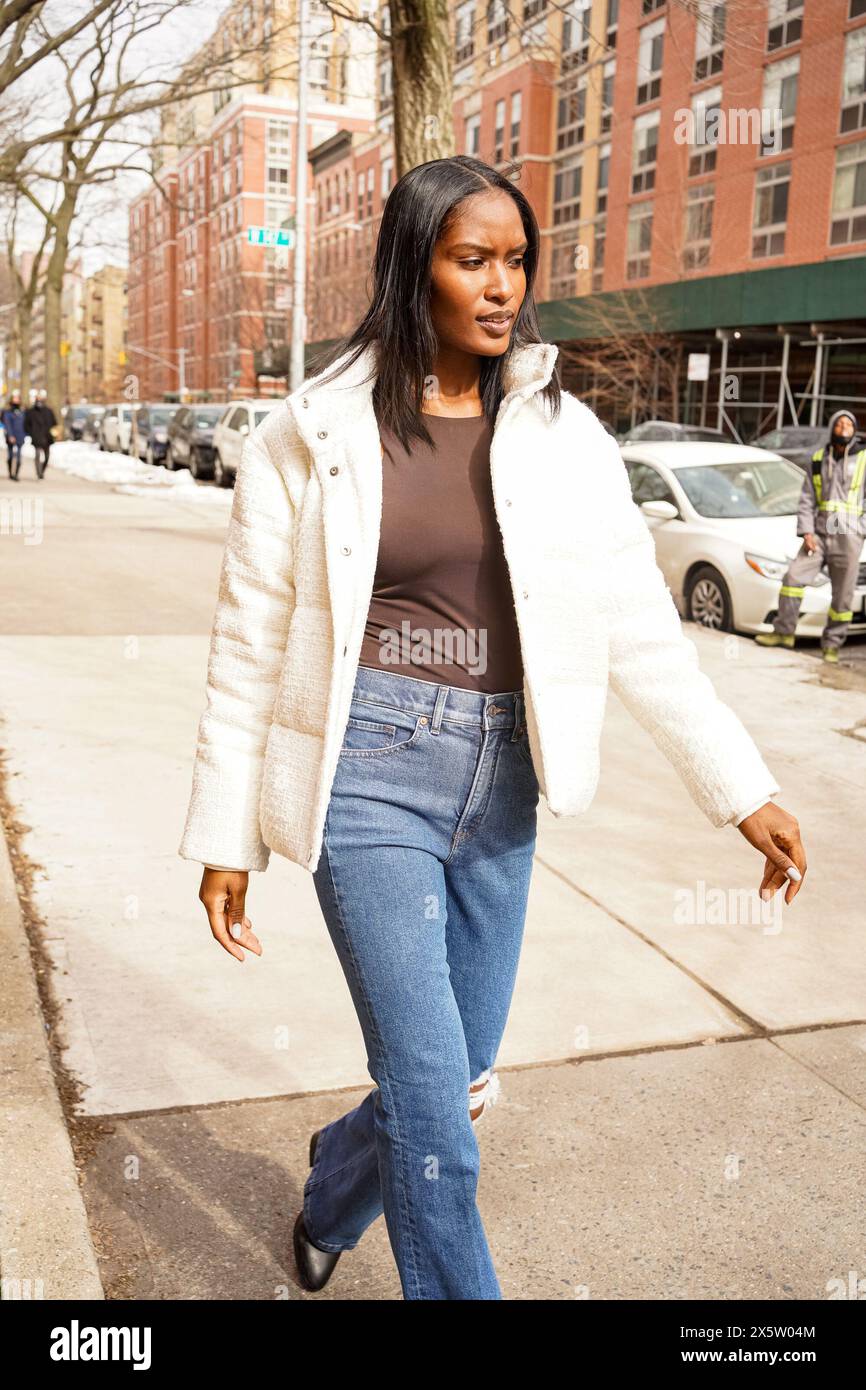 Femme en veste blanche marchant sur le trottoir en ville Banque D'Images