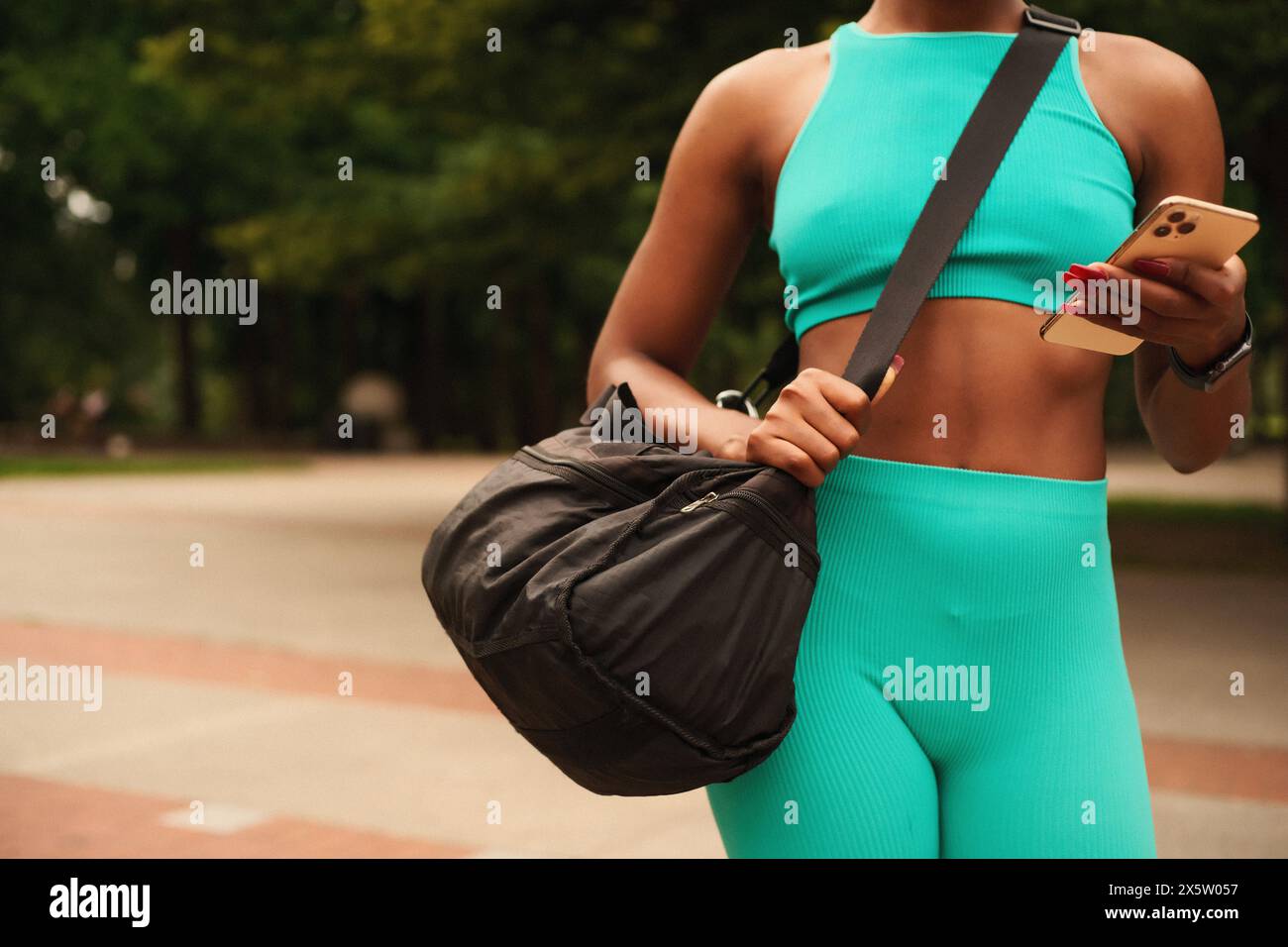 Section médiane de la femme athlète dans les vêtements de sport avec sac de gym et téléphone intelligent Banque D'Images