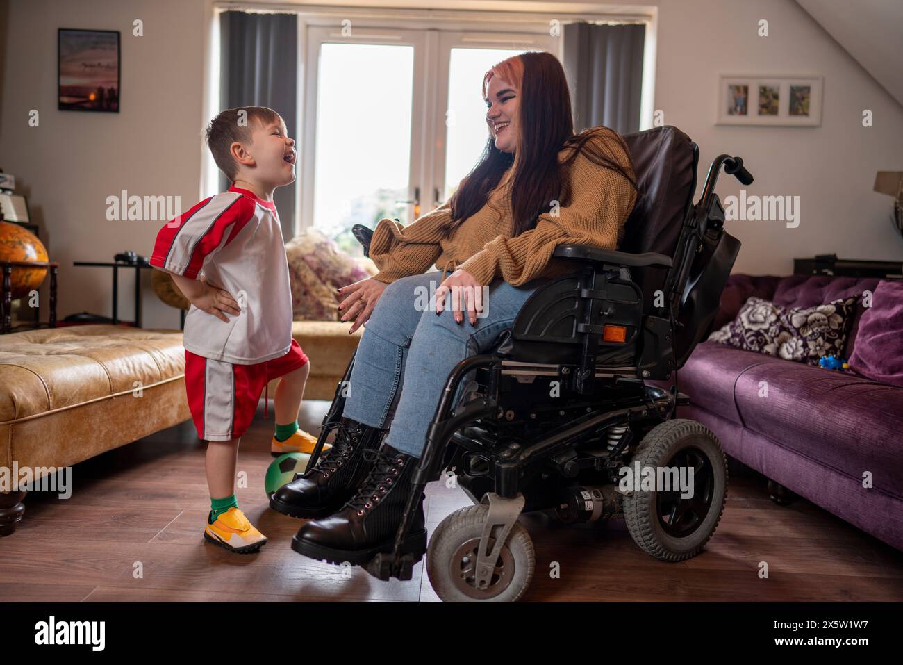 Femme en fauteuil roulant avec fils en uniforme de football dans le salon Banque D'Images Femme en fauteuil roulant avec fils en uniforme de football dans le salon Banque D'Images