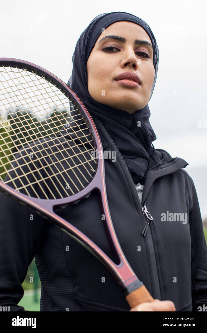 Portrait de femme en vêtements de sport noirs et hijab tenant une raquette de tennis Banque D'Images