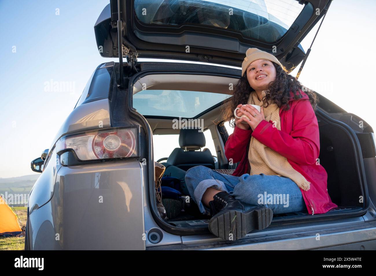 Jeune femme assise dans le coffre de voiture et buvant du thé Banque D'Images
