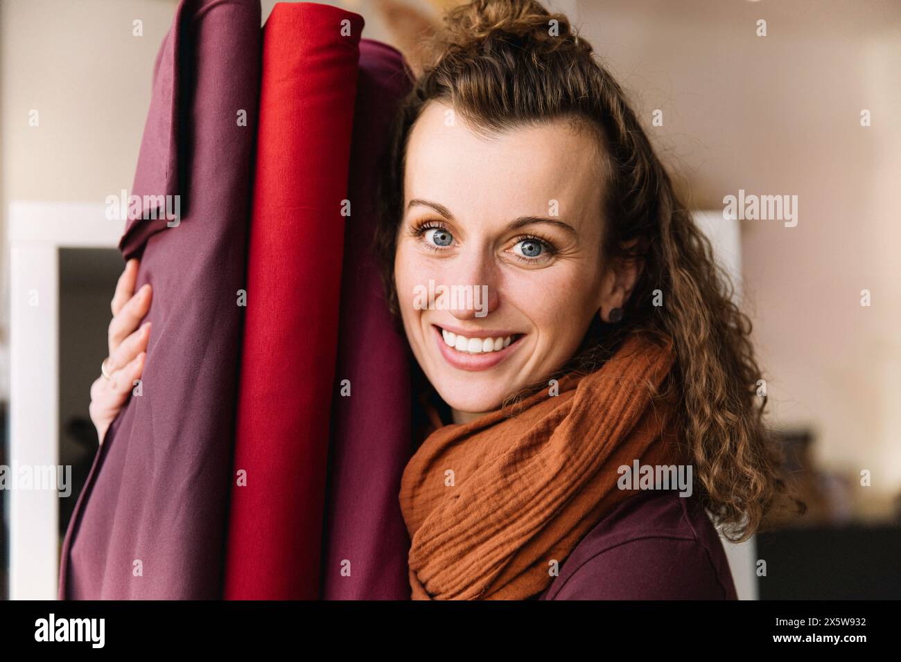 Femme ravie aux cheveux bouclés éclatant de rire, tenant des rouleaux de tissu vibrants Banque D'Images