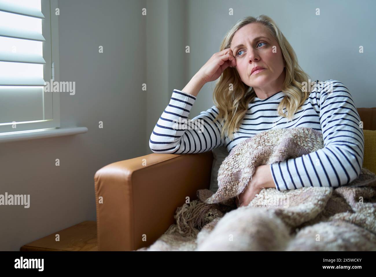 Femme mature économiquement inactive souffrant d'une maladie à long terme assise sur un canapé à la maison Banque D'Images