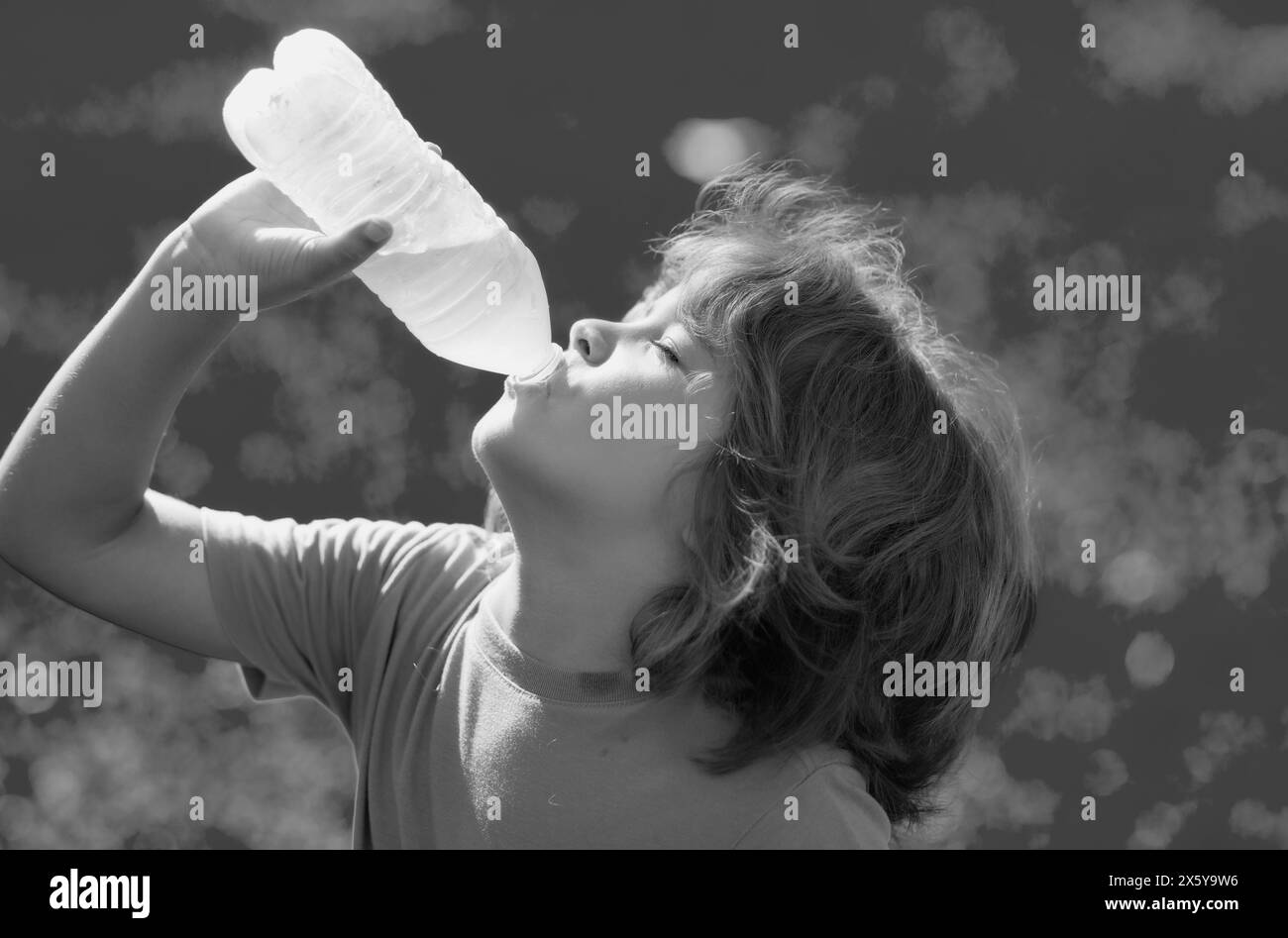 Eau potable pour enfants. Portrait d'un petit enfant souriant heureux avec un verre d'eau douce. Enfant assoiffé. Un garçon en plein air boit une bouteille pure en verre Banque D'Images