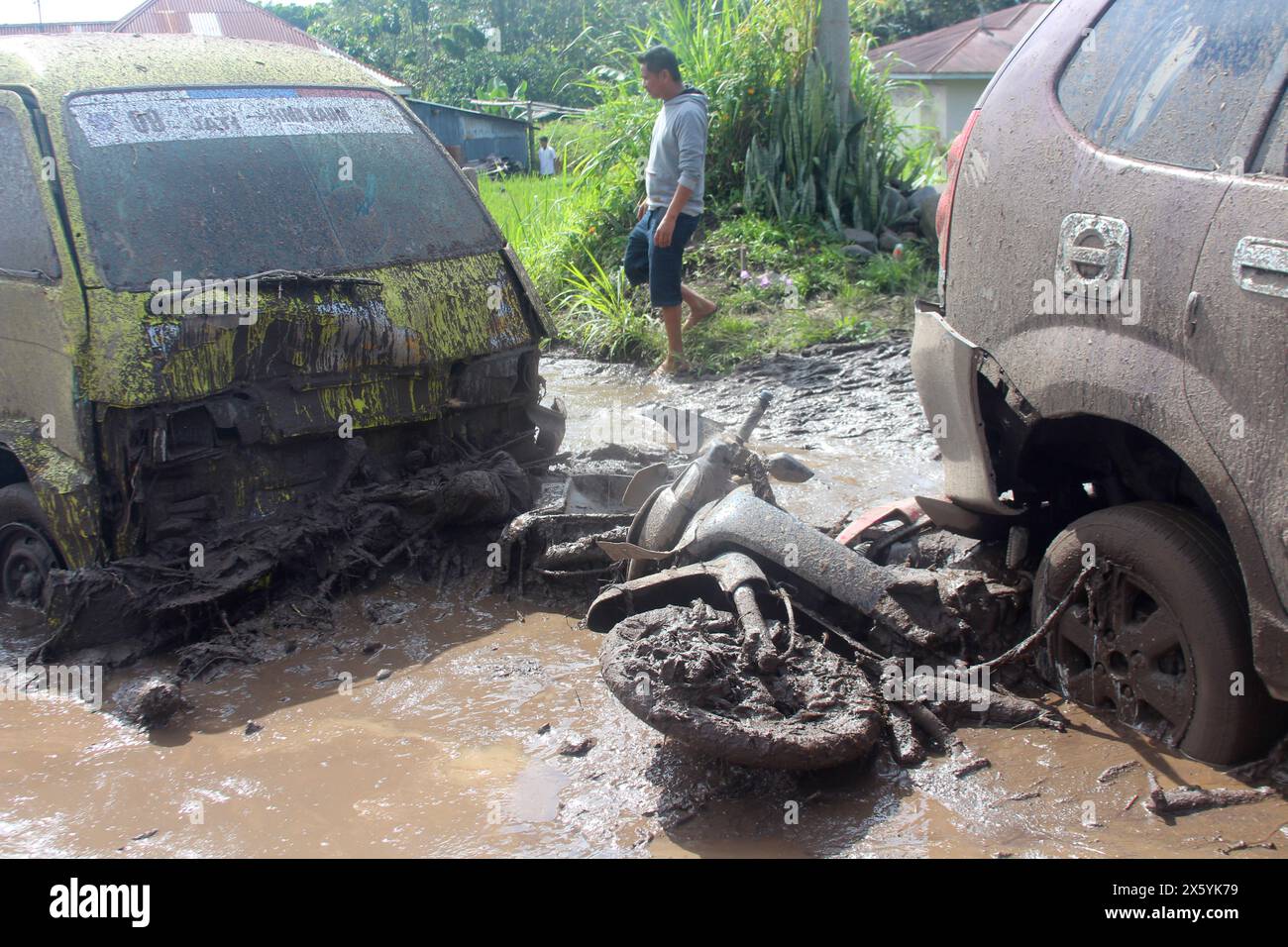 A man walks past the wreckages of cars and a motorcycle swept away by a flash flood in Agam, West Sumatra, Indonesia, Sunday, May 12, 2024. Heavy rains and torrents of cold lava and mud rushing down a volcano on Indonesia’s Sumatra island have triggered flash floods that killed more than a dozen of people and injured several others, officials said Sunday. (AP Photo/Ali Nayaka) Banque D'Images