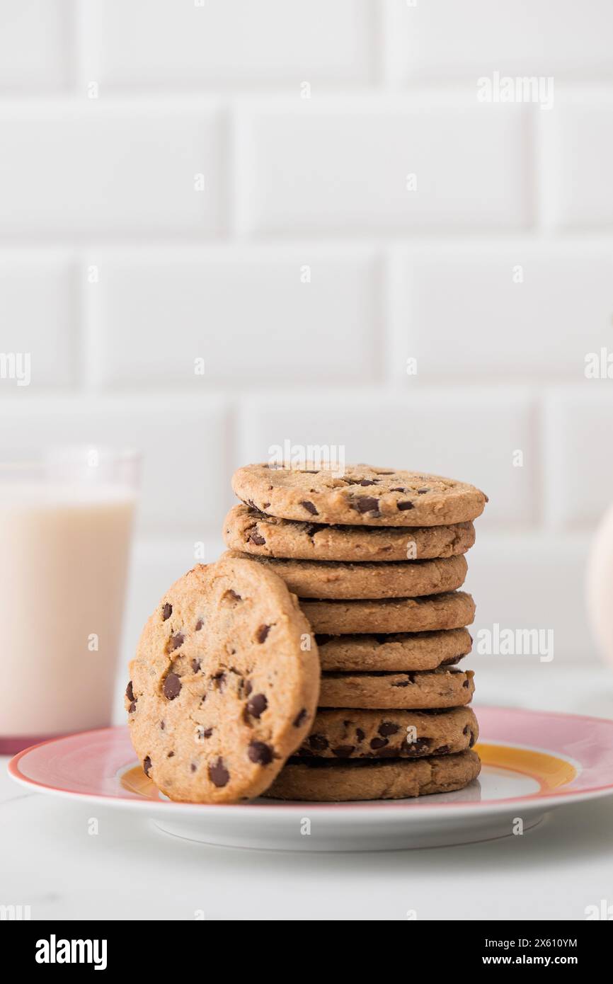 Les biscuits sont étalés sur une assiette, un verre de lait frais. Biscuits faits maison avec pépites de chocolat. Banque D'Images