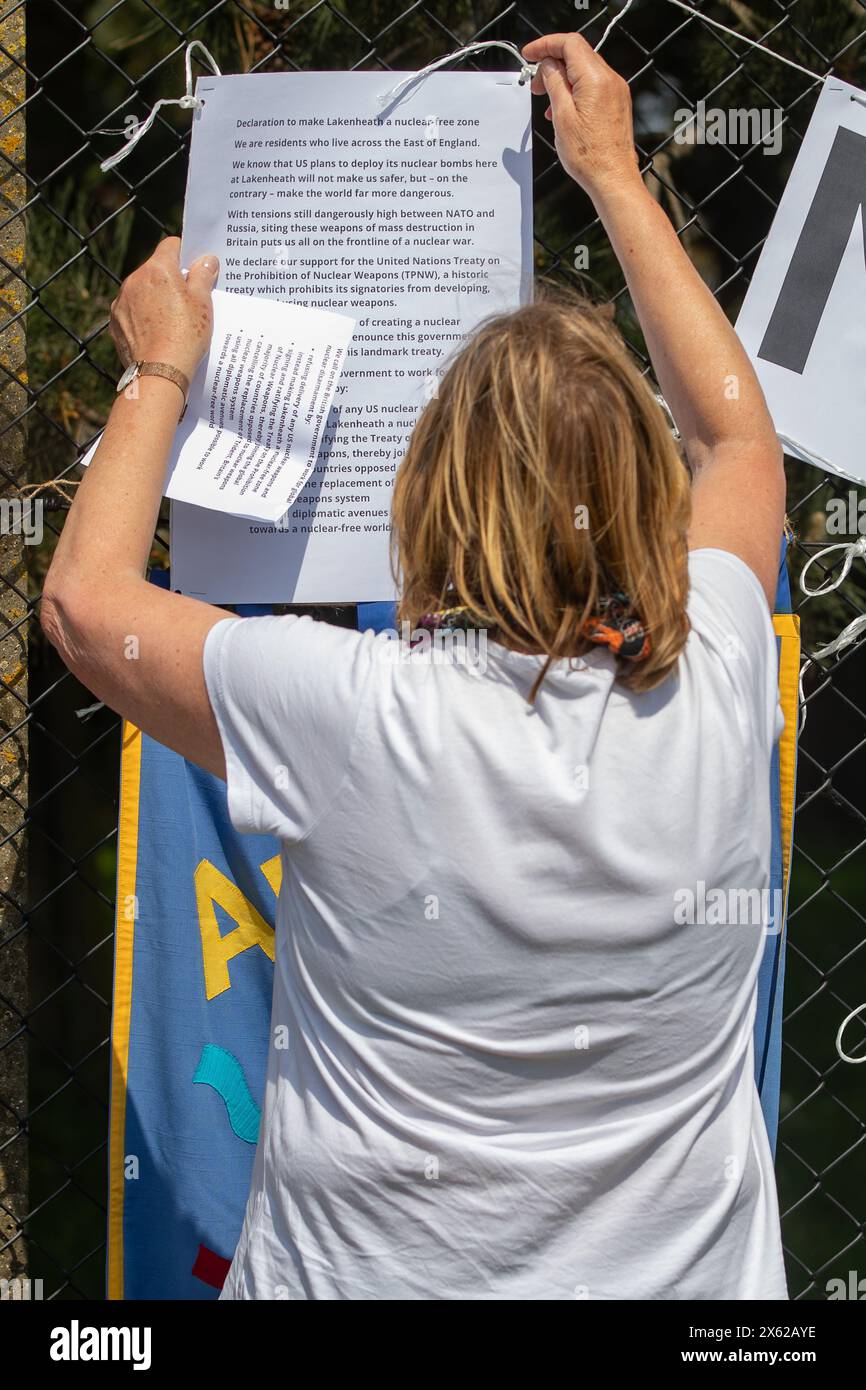 Lakenheath, Royaume-Uni. 11 mai 2024. Sue Wright de Norwich CND fixe un avis sur la clôture de périmètre de la RAF Lakenheath déclarant qu'elle est une zone exempte d'armes nucléaires lors d'une manifestation de la campagne pour le désarmement nucléaire (CND) devant la base. Les manifestants ont appelé le gouvernement britannique à refuser la livraison de bombes nucléaires américaines B61-12 à la base. Il faisait partie d'une journée nationale d'action de la CND. Crédit : Mark Kerrison/Alamy Live News Banque D'Images