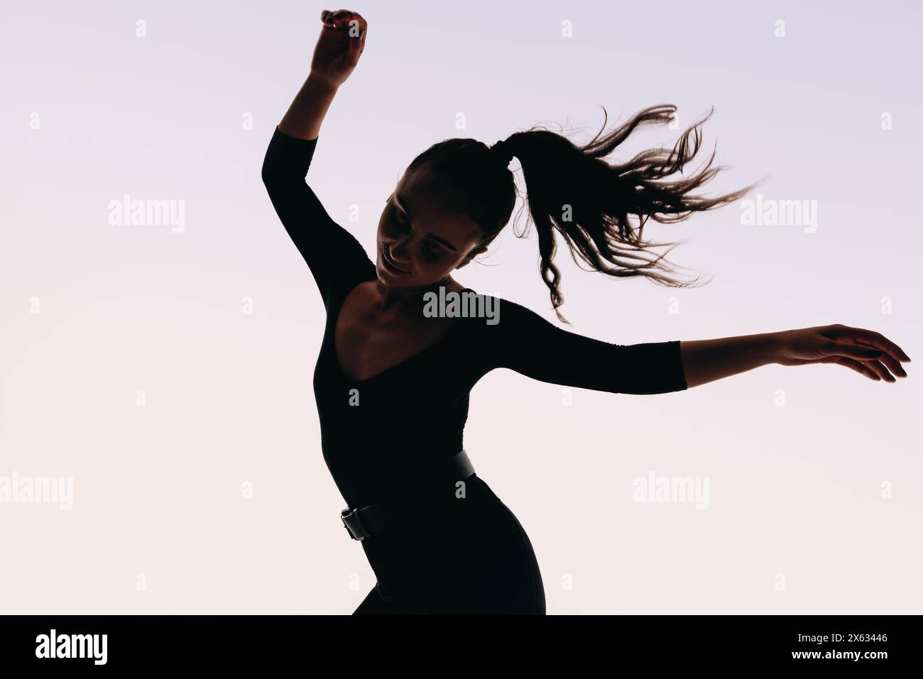 Femme avec une queue de cheval et un physique tonique danse en toute confiance dans un studio blanc. Ses mouvements dynamiques et athlétiques, son langage corporel expressif et artistique Banque D'Images