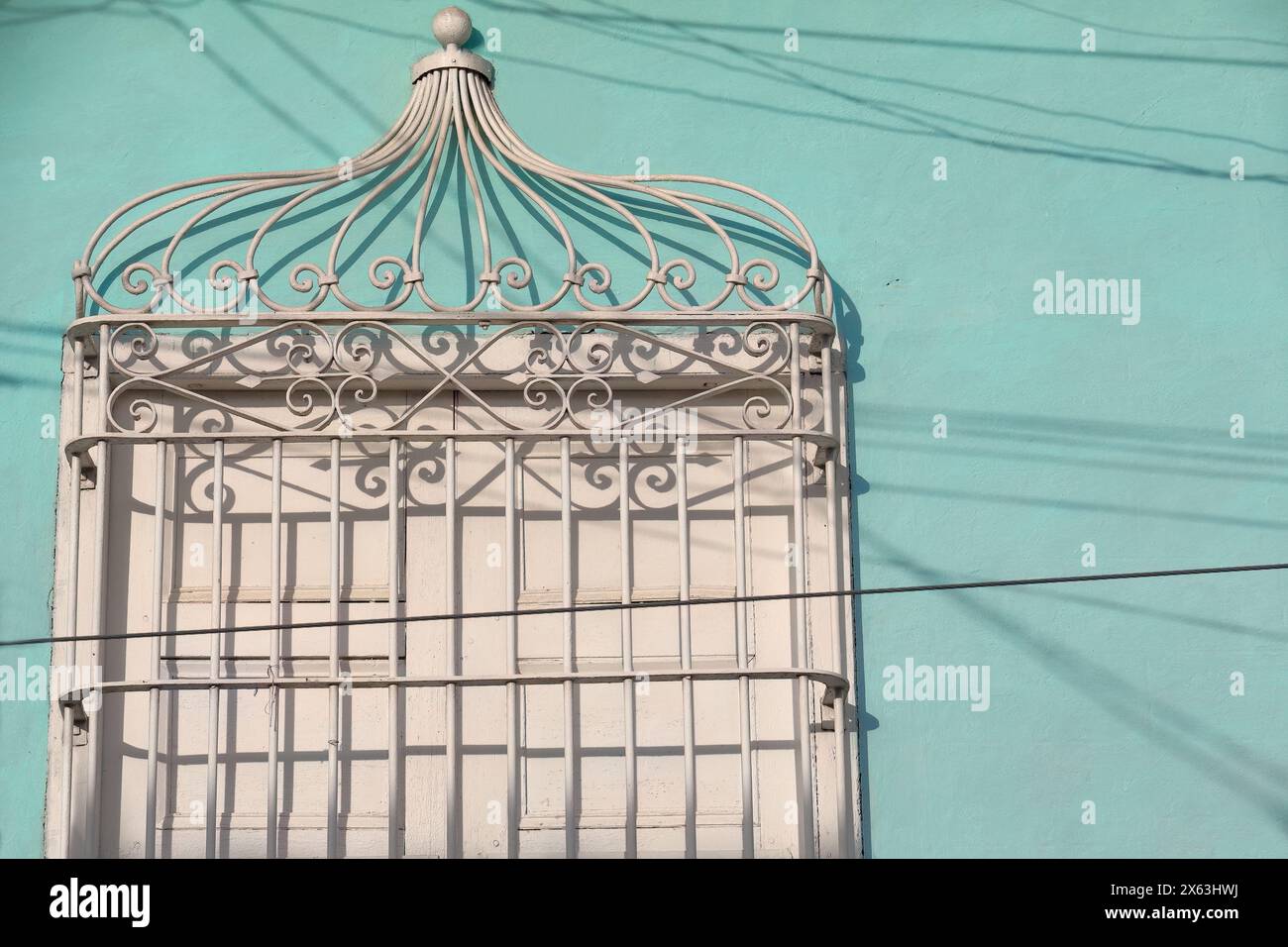 269 le soleil de fin d'après-midi illumine pleinement la grille d'une fenêtre avec volets en bois blanc fermés, mur vert menthe d'une maison coloniale. Trinidad-Cuba. Banque D'Images