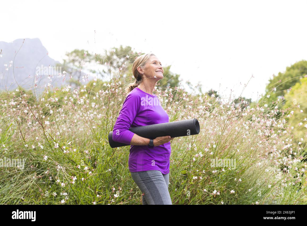 À l'extérieur, femme âgée caucasienne tenant un tapis de yoga, profitant de la nature Banque D'Images