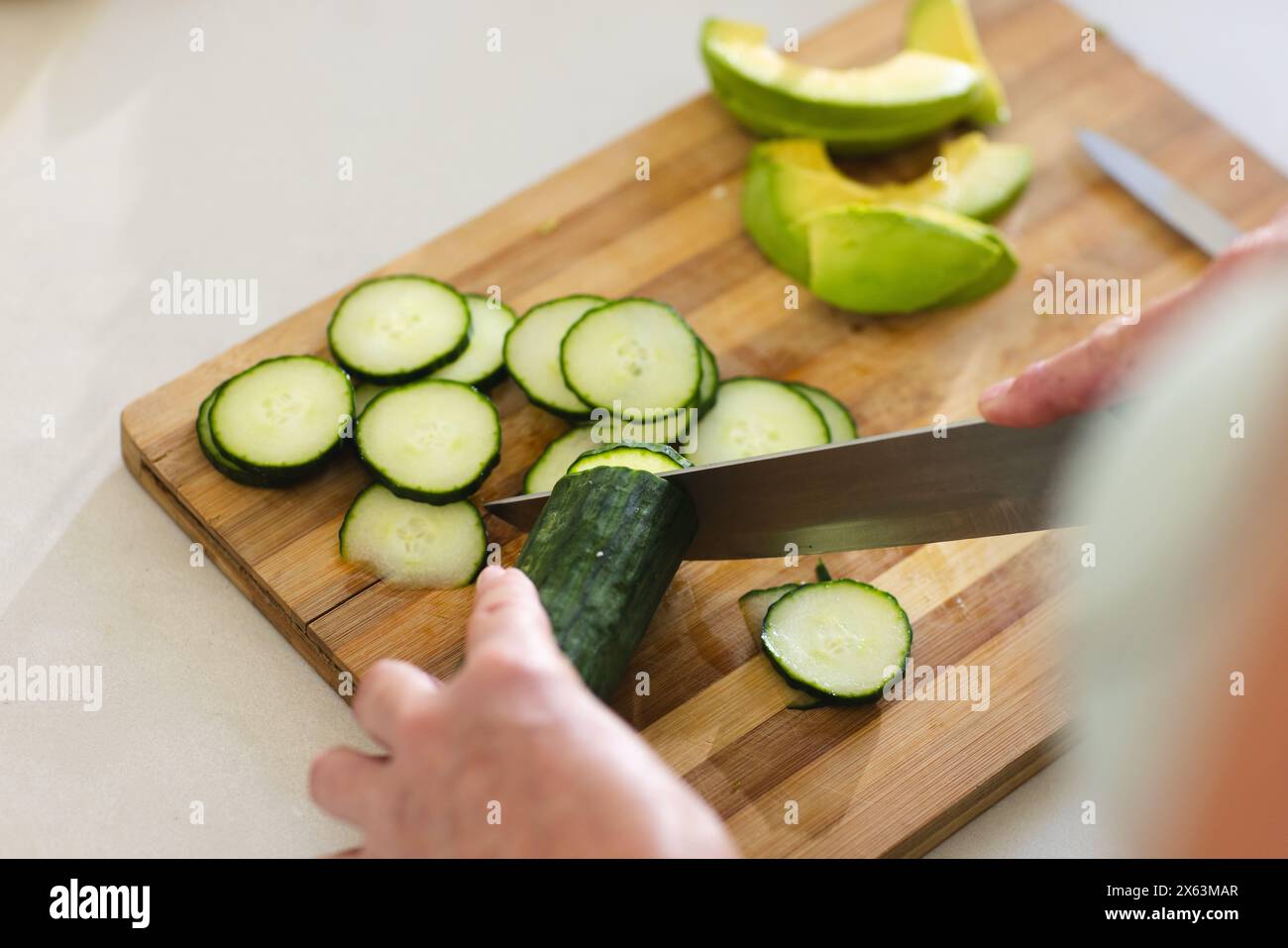 À la maison, femme caucasienne mature tranchant le concombre, avocat à proximité Banque D'Images