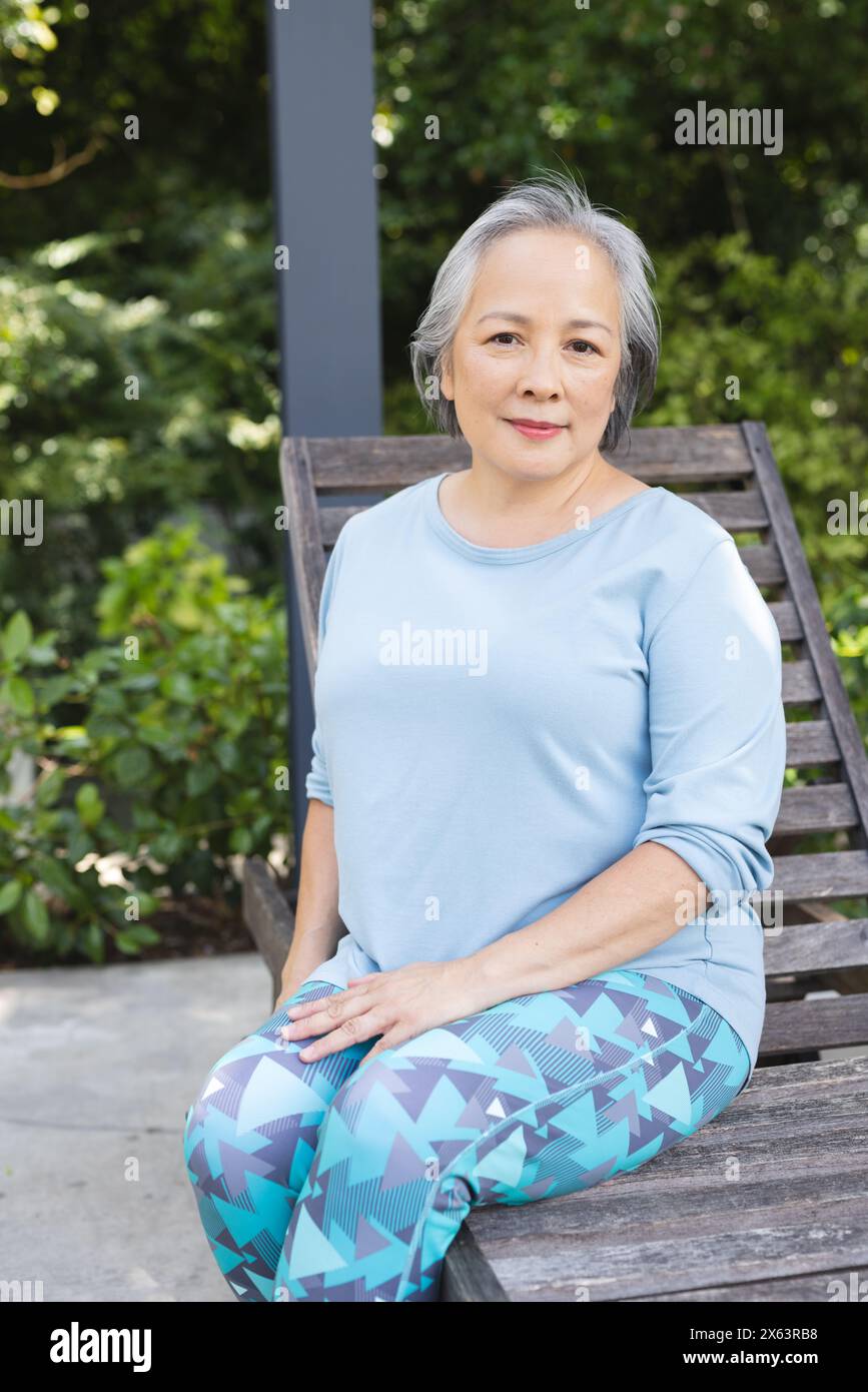 À l'extérieur, femme asiatique senior assise sur un banc en bois Banque D'Images
