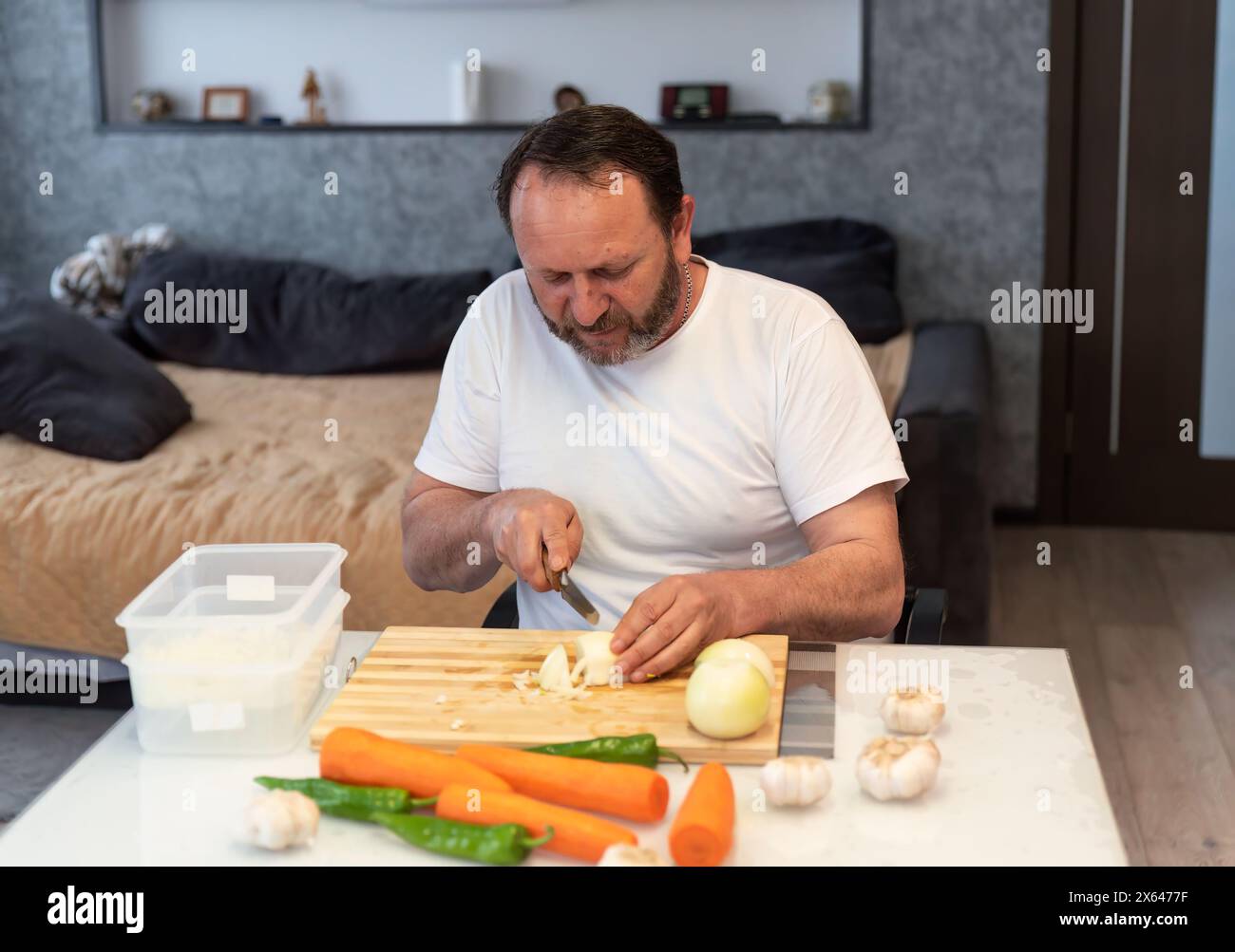 Homme mûr cuisinant pilaf, coupant des légumes dans la cuisine à la maison Banque D'Images