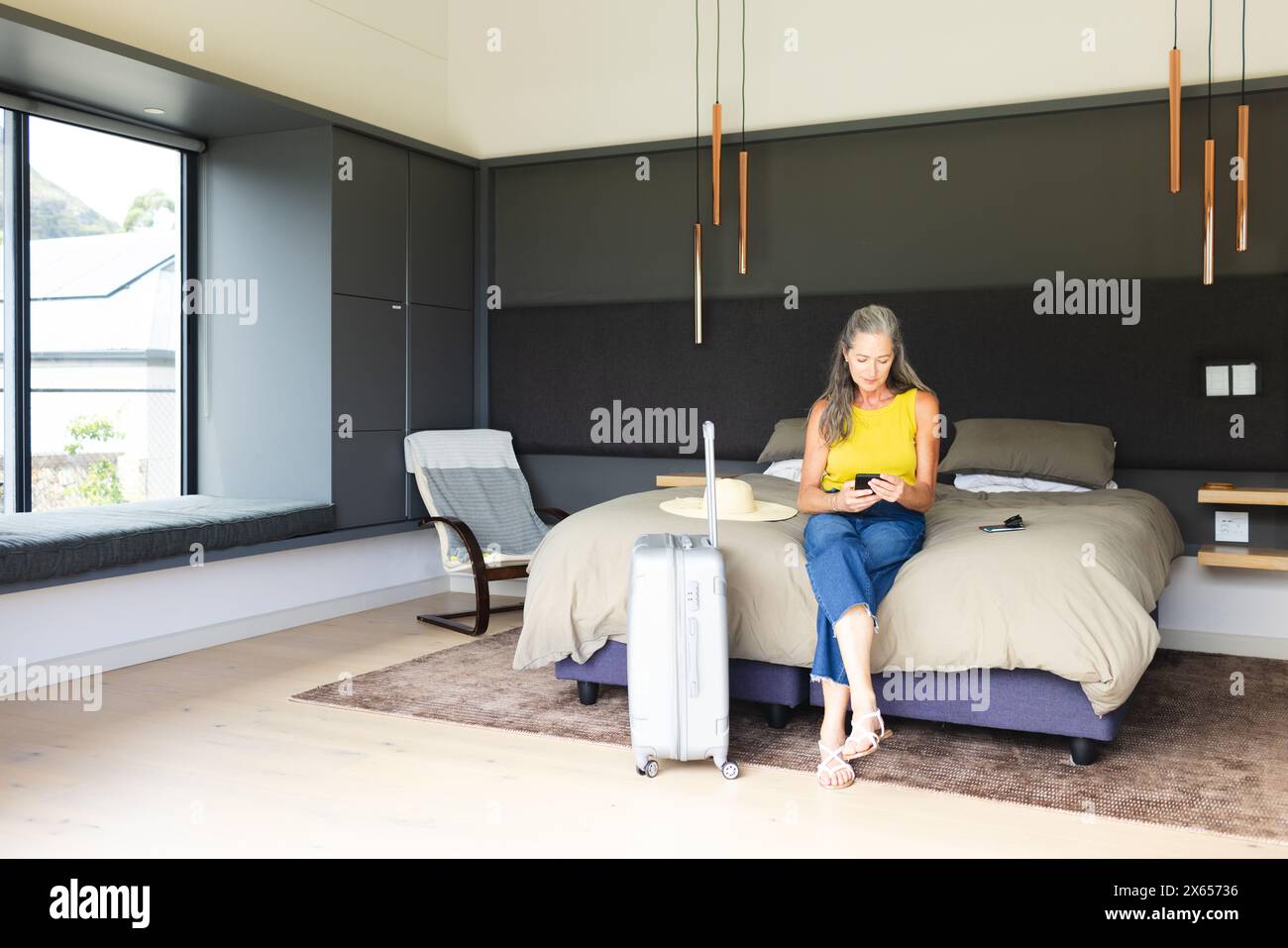 À la maison, femme caucasienne mature assise sur le lit, regardant un smartphone Banque D'Images