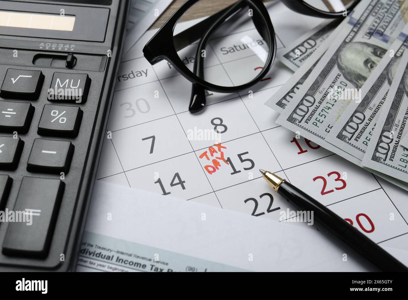Calendrier avec rappel de date sur le jour des impôts, documents, argent, stylo, calculatrice et lunettes sur la table, gros plan Banque D'Images